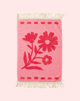 A light and dark pink hand towel with a floral pattern and fringe detailing on two ends. 