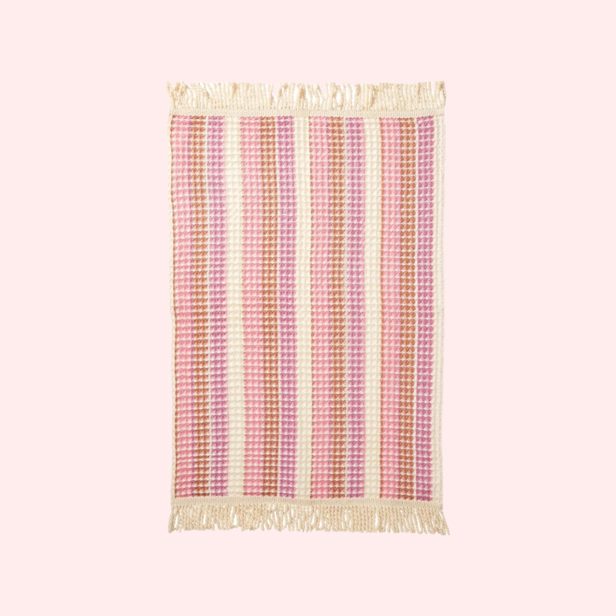 A pink and ivory striped waffle knit hand towel with tassel detailing on each end. 