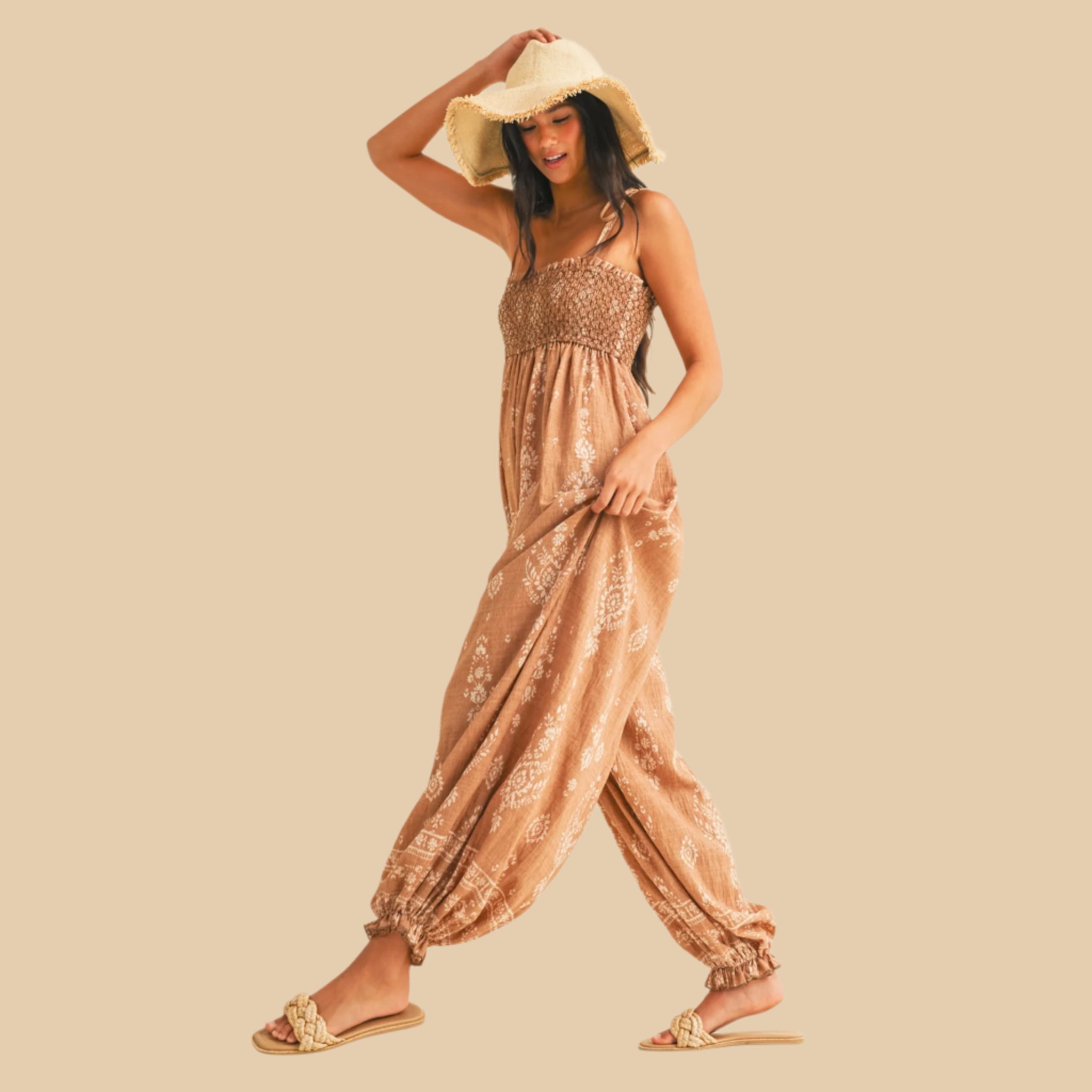 A taupe balloon leg jumpsuit with spaghetti shoulder straps and an ivory print. 