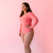 A model wearing a coral one piece long-sleeve surf swimsuit. 