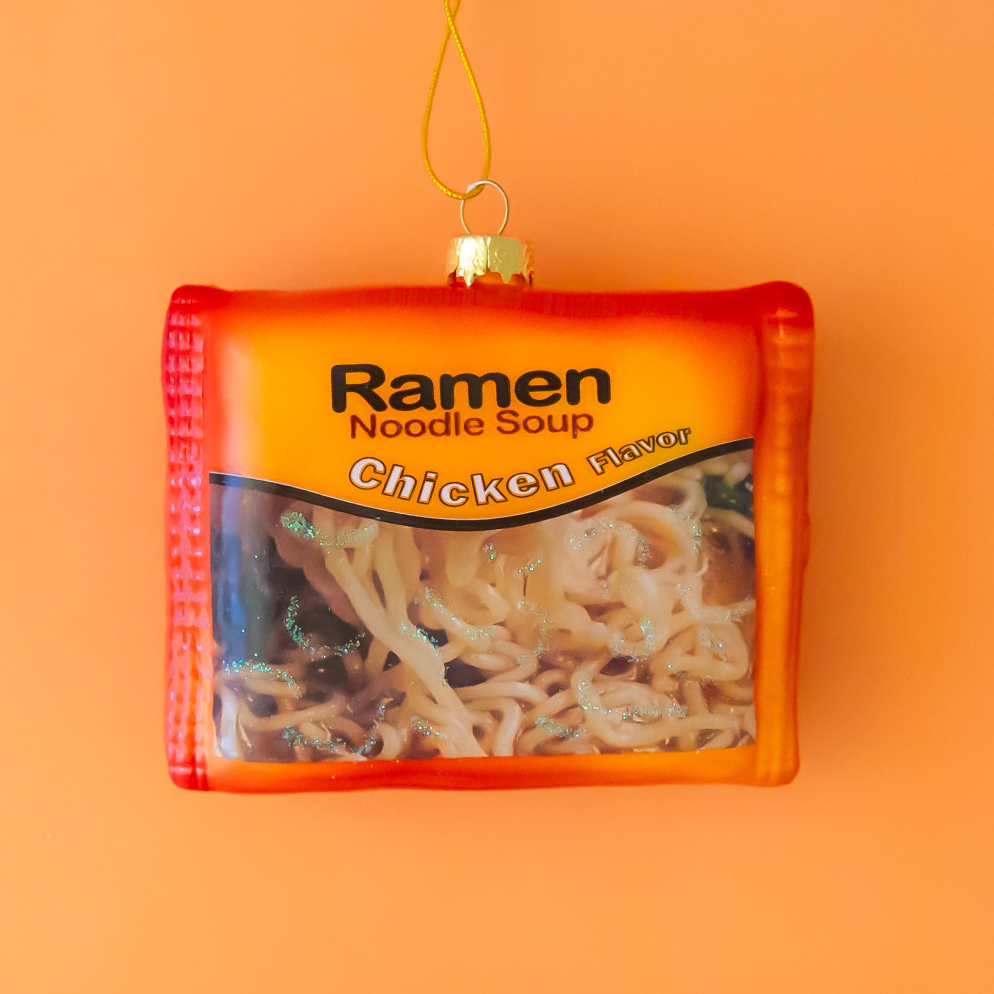 An orange ramen package shaped ornament with text that reads, 'Ramen Noodle Soup Chicken'.