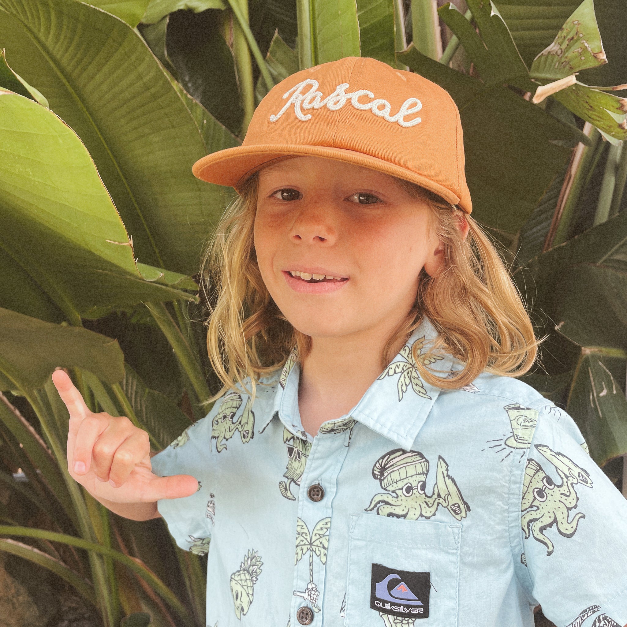 A burnt orange flat brimmed hat with white embroidered text that reads, &quot;Rascal&quot;.