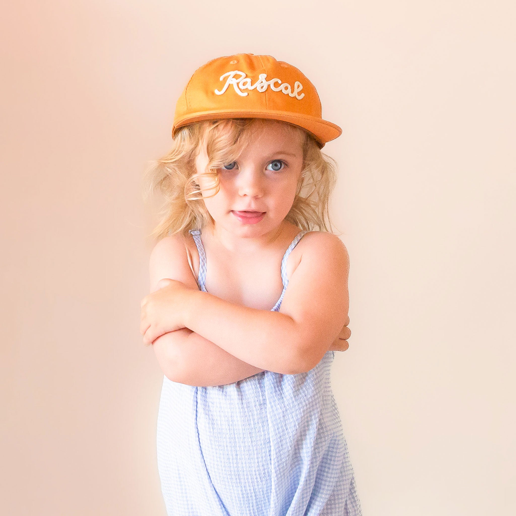 A burnt orange flat brimmed hat with white embroidered text that reads, &quot;Rascal&quot;.