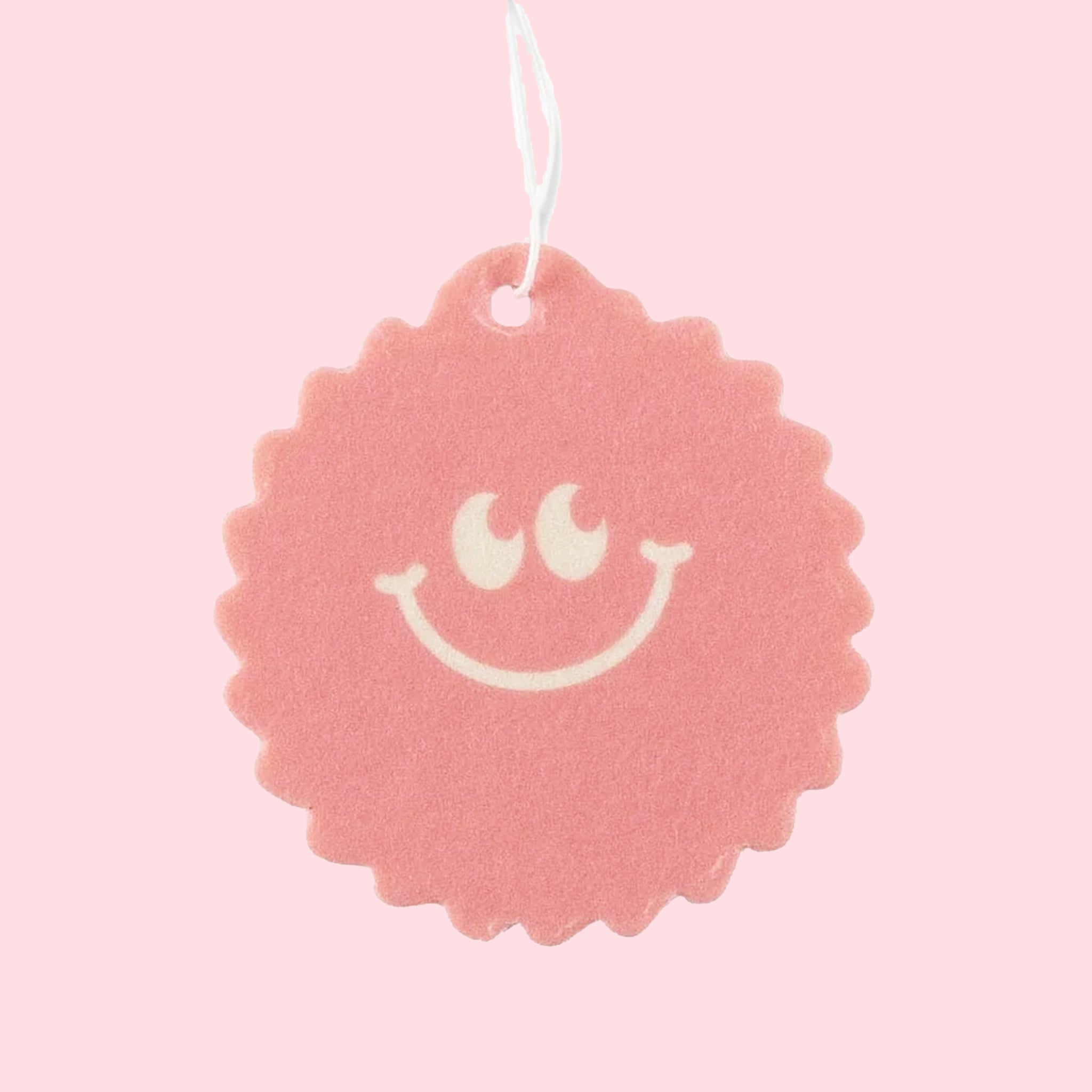 On a pink background is a pink sun shaped air freshener with a smiley face. 