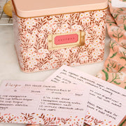 A metal recipe box with a pink daisy pattern with recipe cards and dividers. 