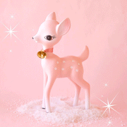 On a pink background is a retro deer shaped figurine in a pink shade with a gold bell around its neck and white spot details. 