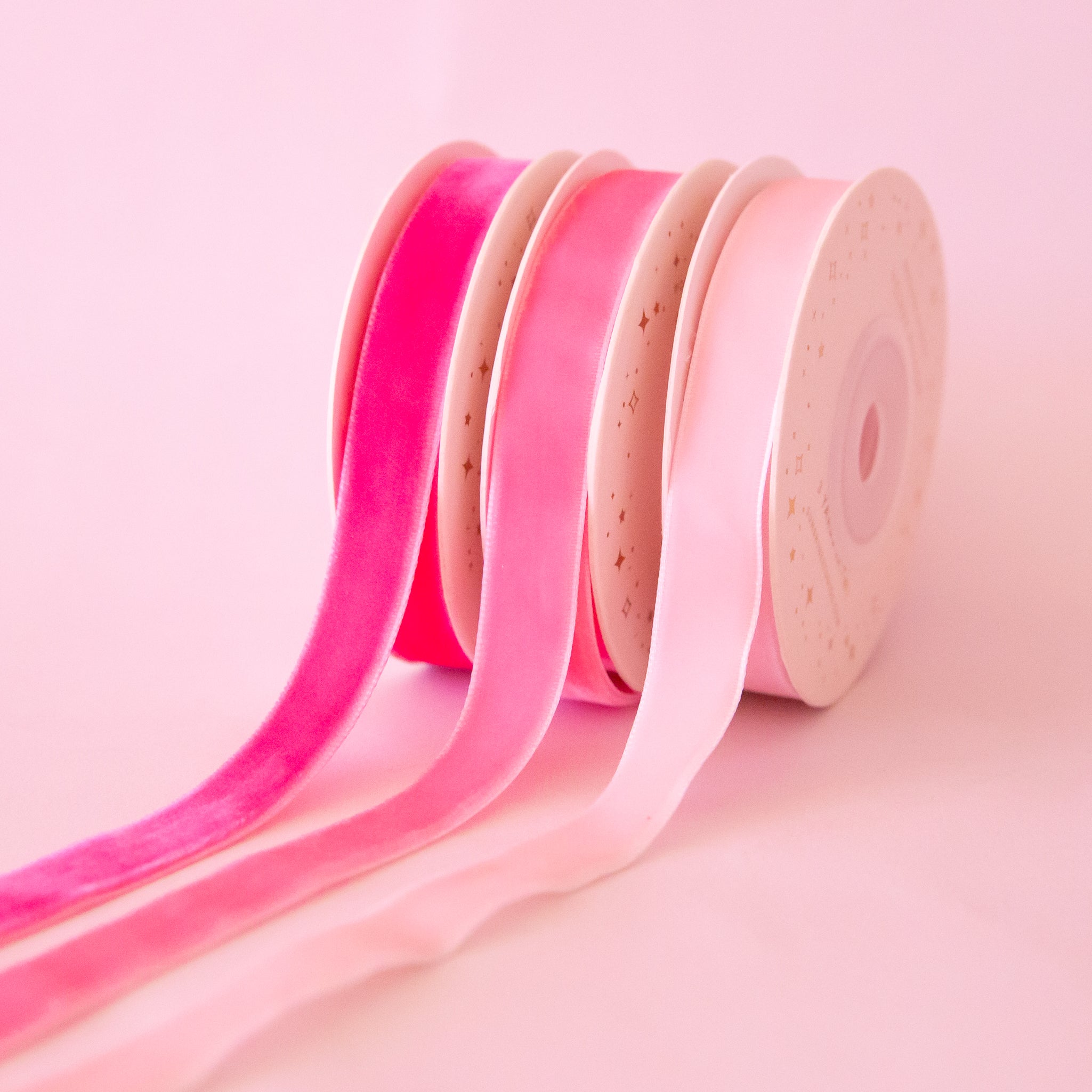 On a pink background is a pack of three pink velvet ribbon spools. 