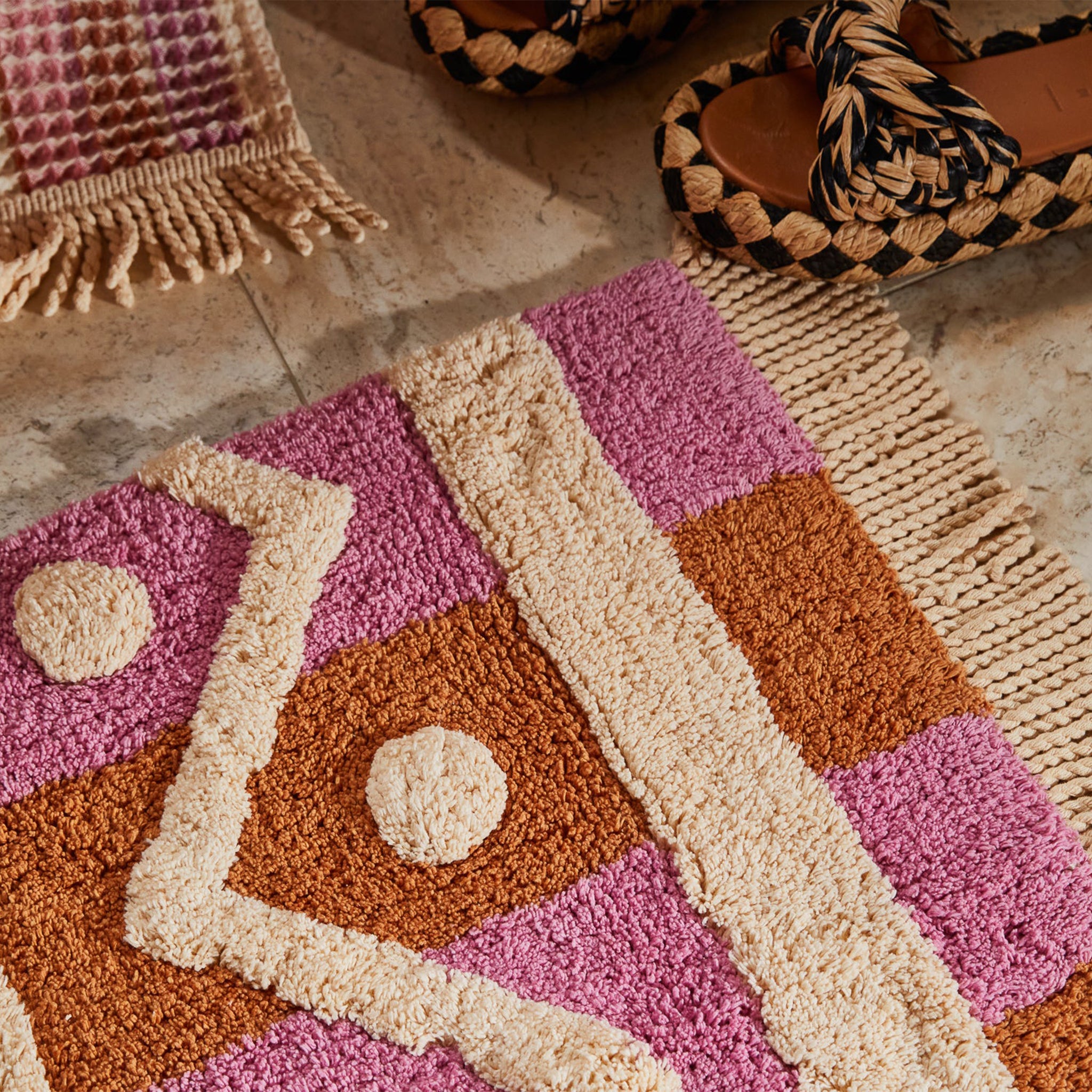 A pink, orange and ivory tufted bath mat with a geometric pattern and tassel details on two ends. 