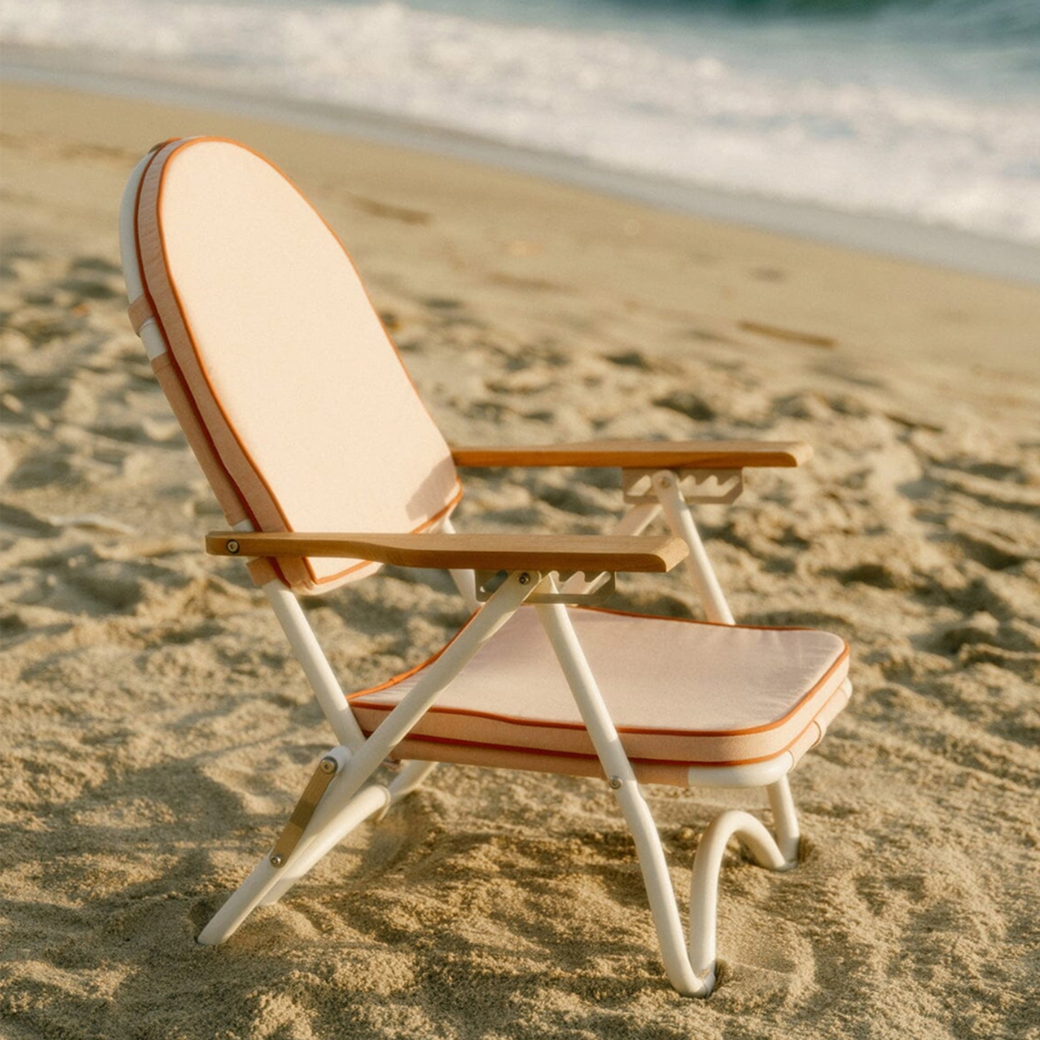 A pink arched folding beach chair with a reddish/dark pink lining around the edge and wood arm rests.