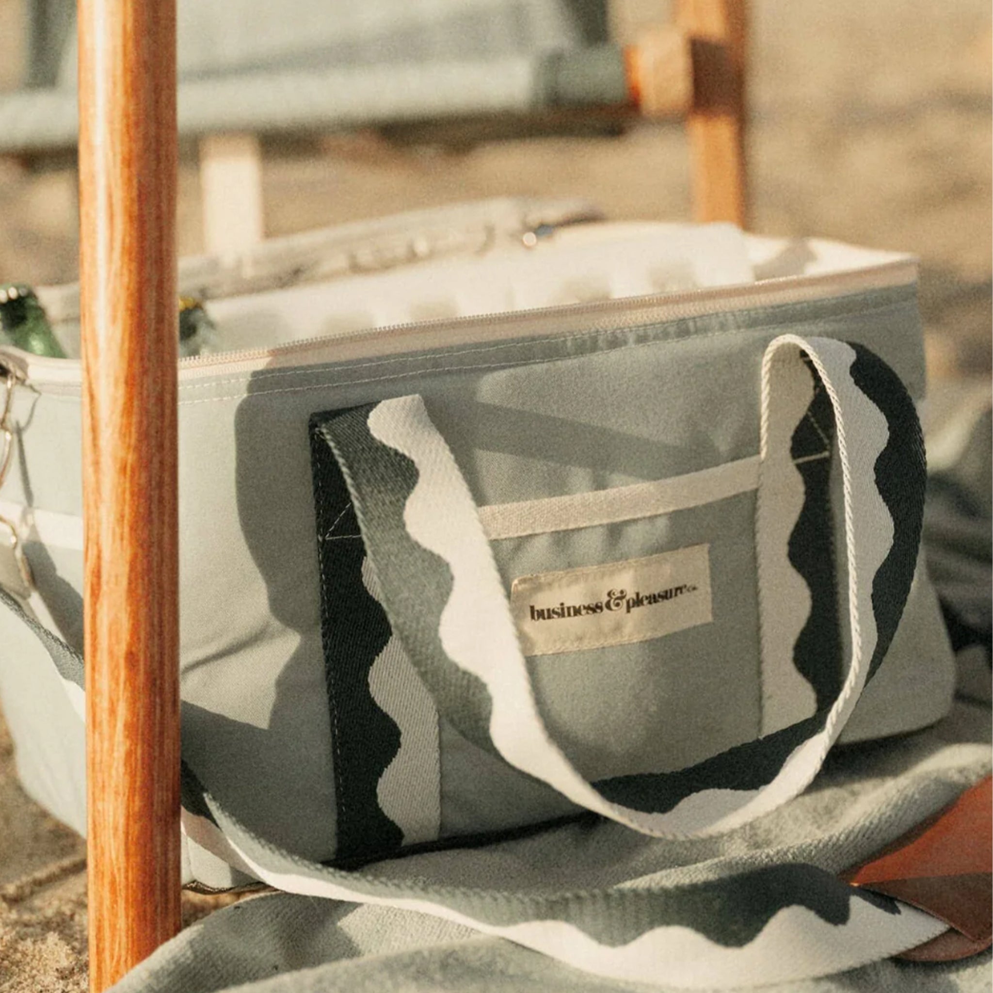 A green premium cooler bag with wavy dark green and white stripes and a label on the front that reads, &quot;business &amp; pleasure&quot;.  