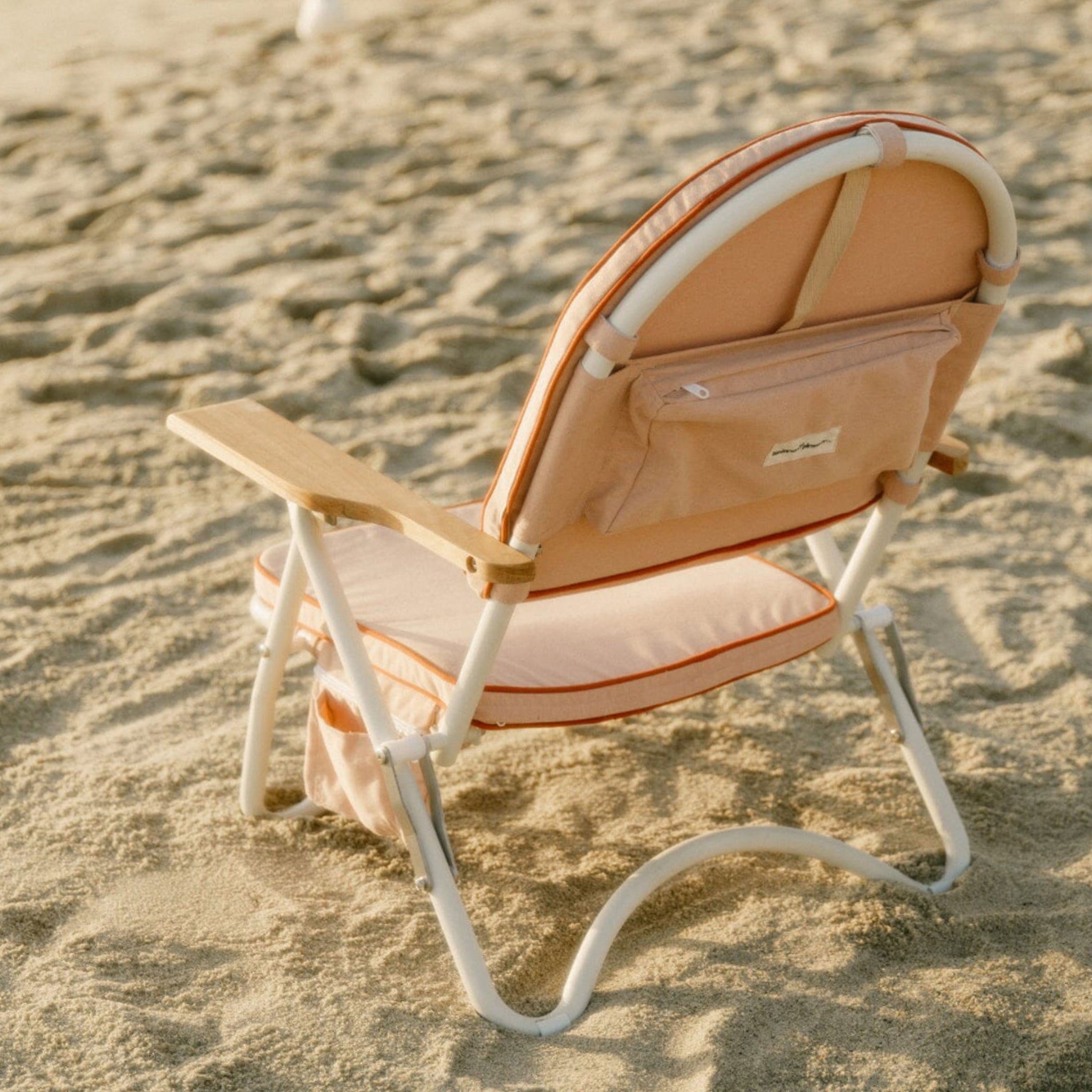 A pink arched folding beach chair with a reddish/dark pink lining around the edge and wood arm rests.