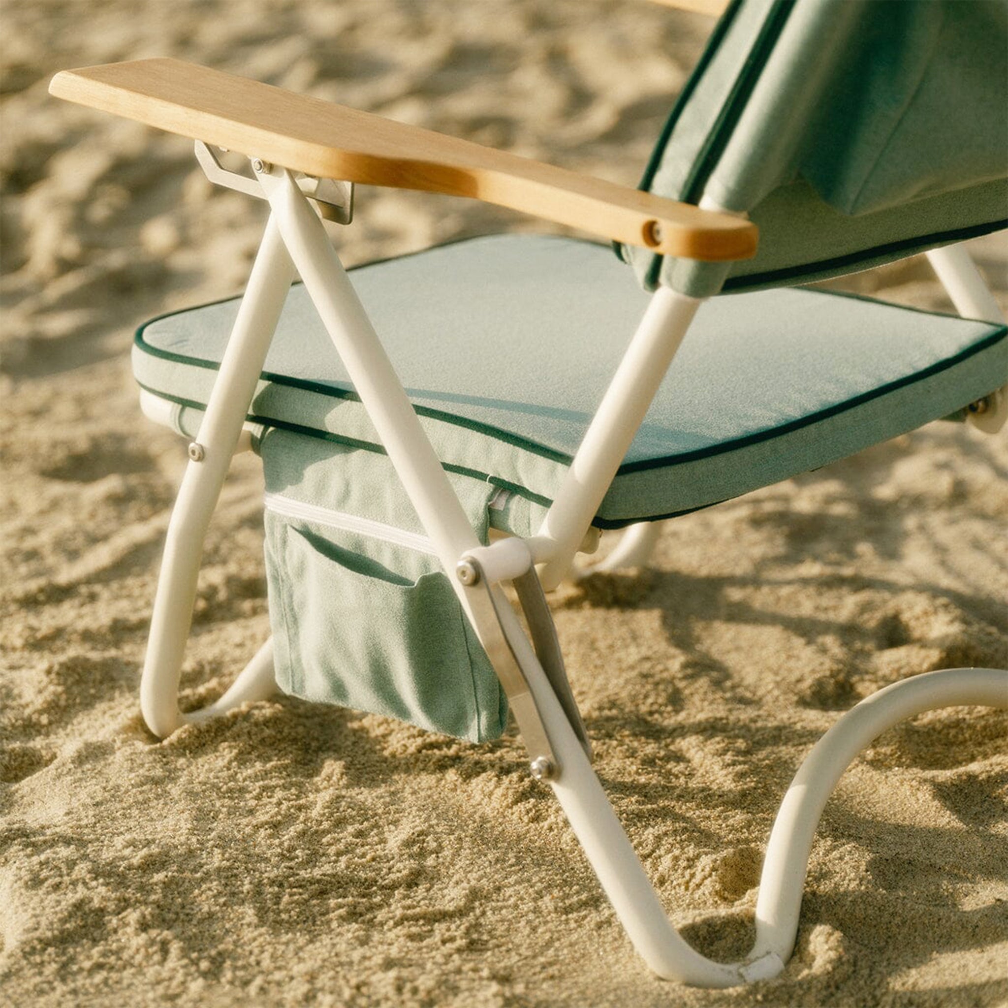 A green arched folding beach chair with wood arm rests and a zipper pocket in the back.