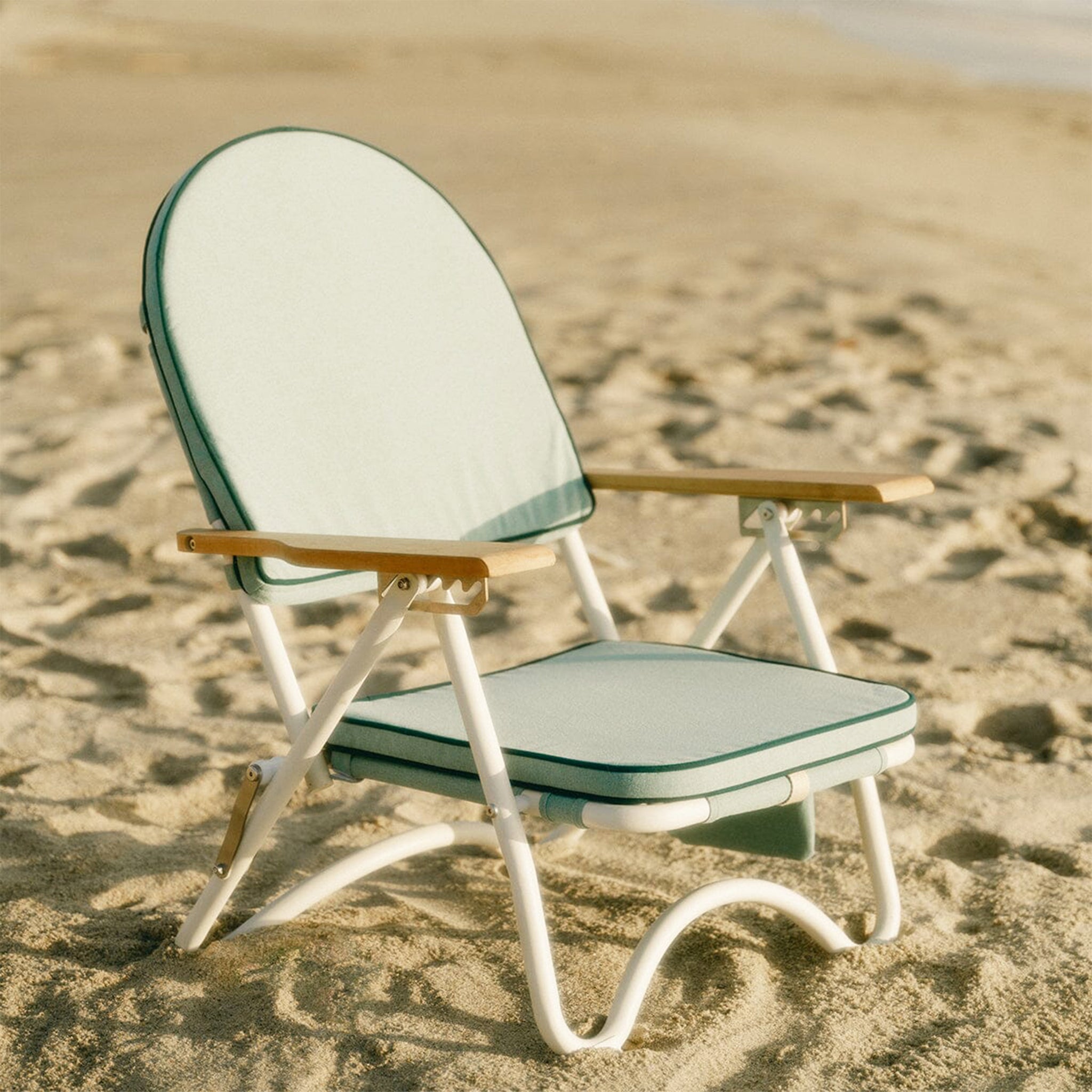 A green arched folding beach chair with wood arm rests and a zipper pocket in the back. 
