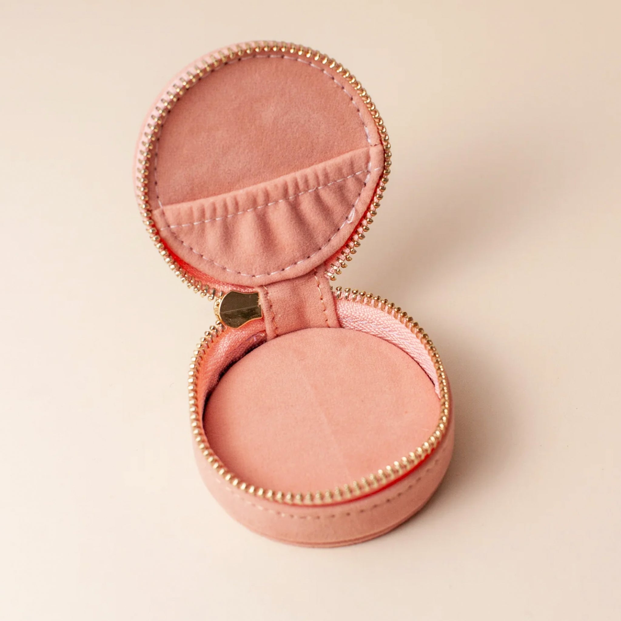 A rose colored circular jewelry case with a gold zipper and a sun design.