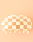 On a peachy background is an ivory and clear checker printed claw clip with a rounded edge.