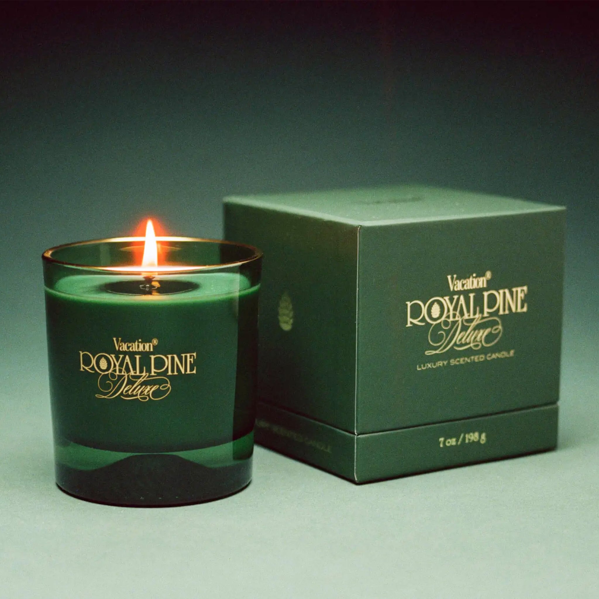 A green glass candle with with gold text that reads, &#39;Vacation Royal Pine Deluxe&#39;. 