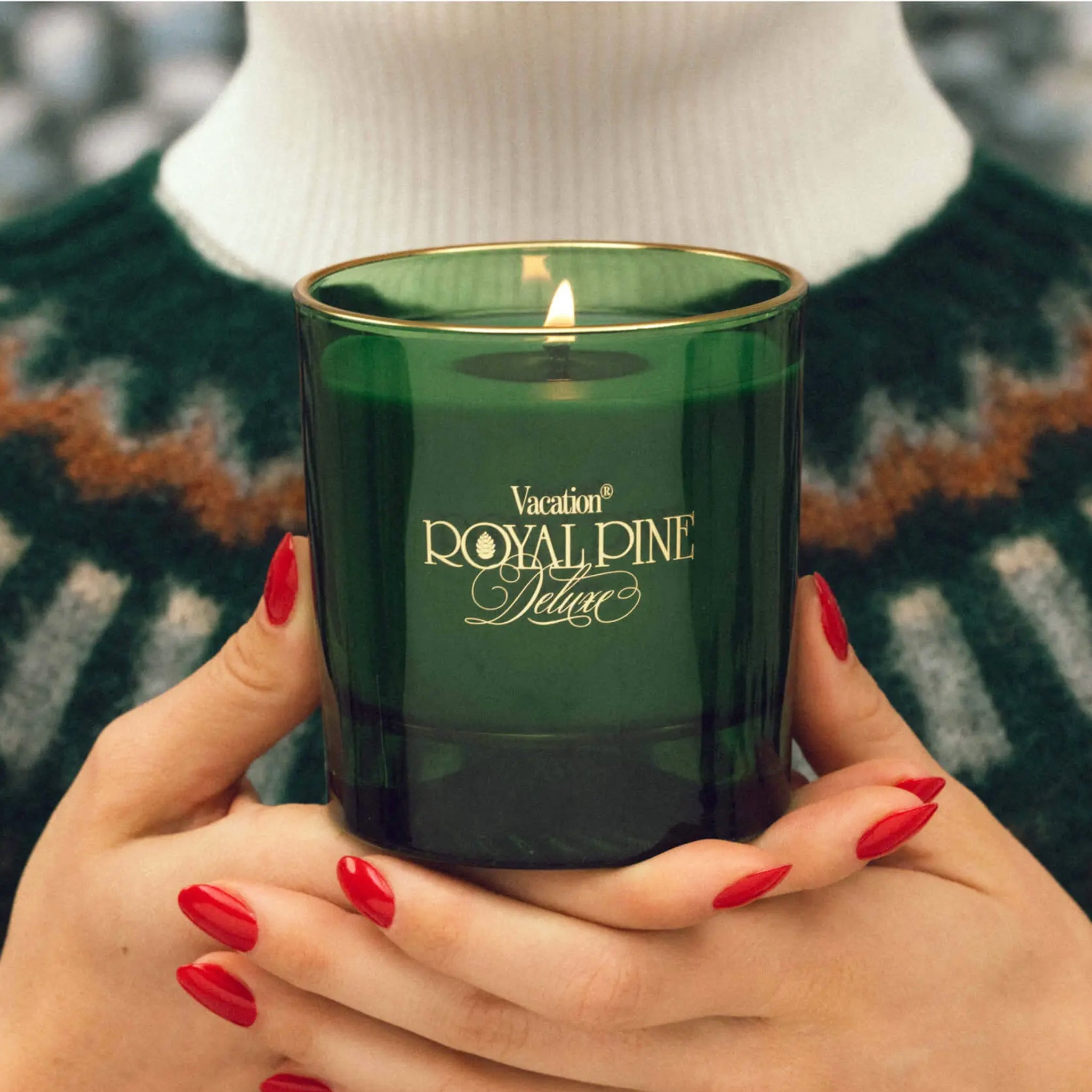 A green glass candle with with gold text that reads, 'Vacation Royal Pine Deluxe'. 