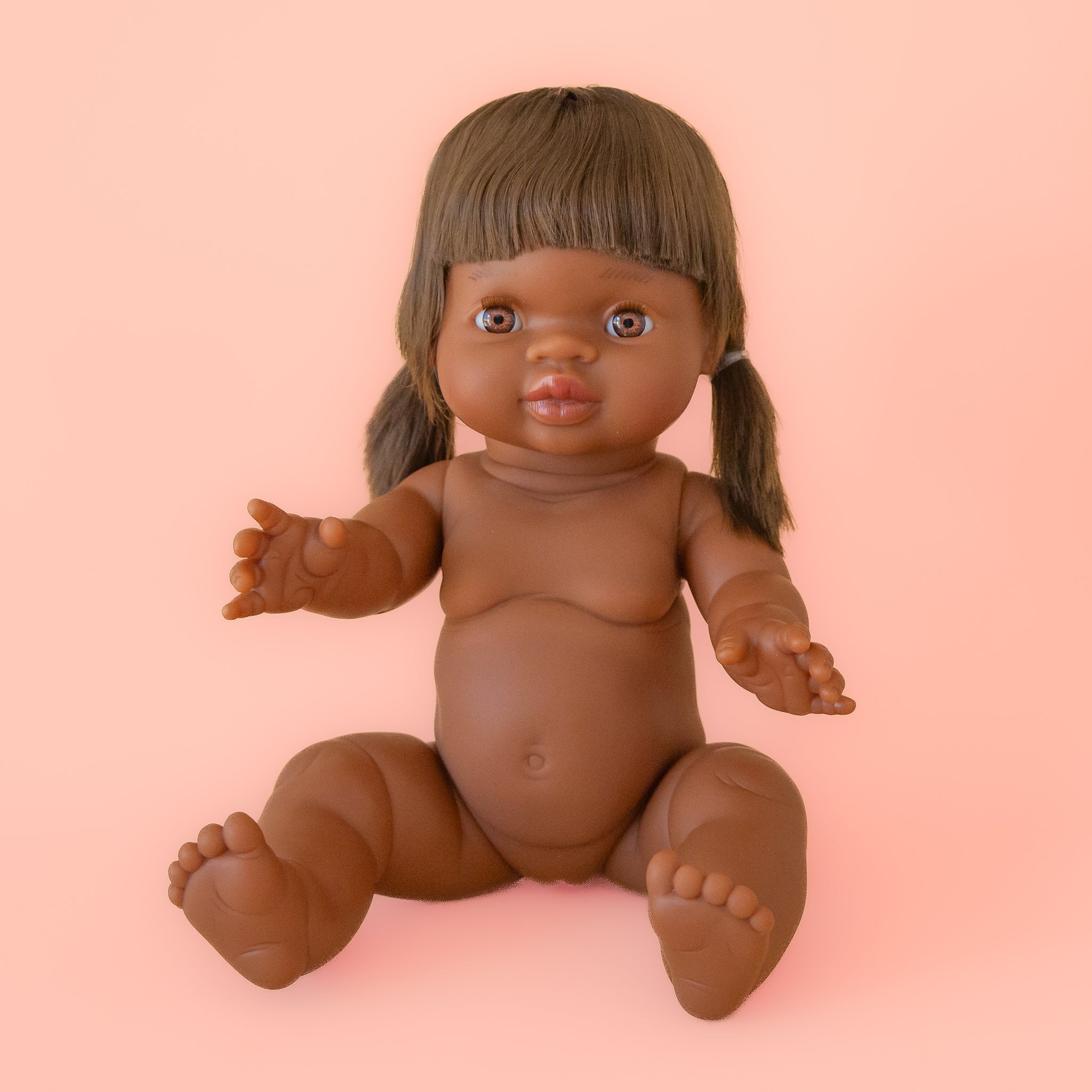 A baby girl doll with light brown eyes and brown pigtail hair. 