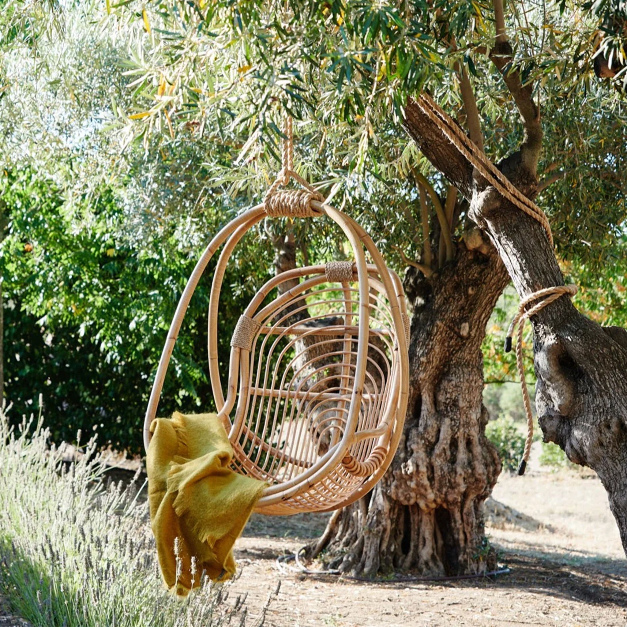  A natural rattan egg shaped hanging chair with an ivory cushion and rope details.