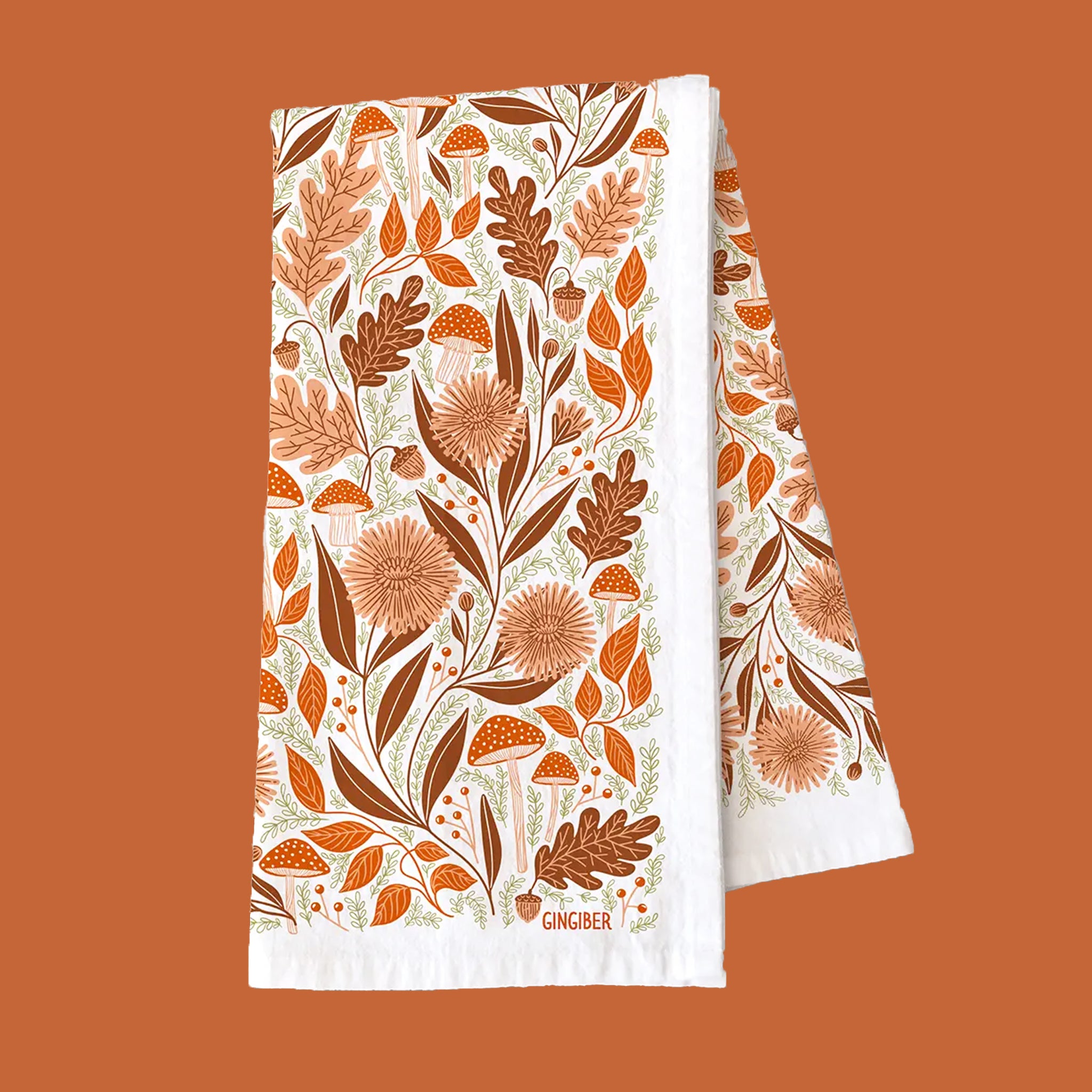 A white cotton kitchen towel with an orange woodland and floral design. 