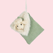 A sheep and sleeping bag shaped green ornament made of wool and felt with a string loop for hanging. 