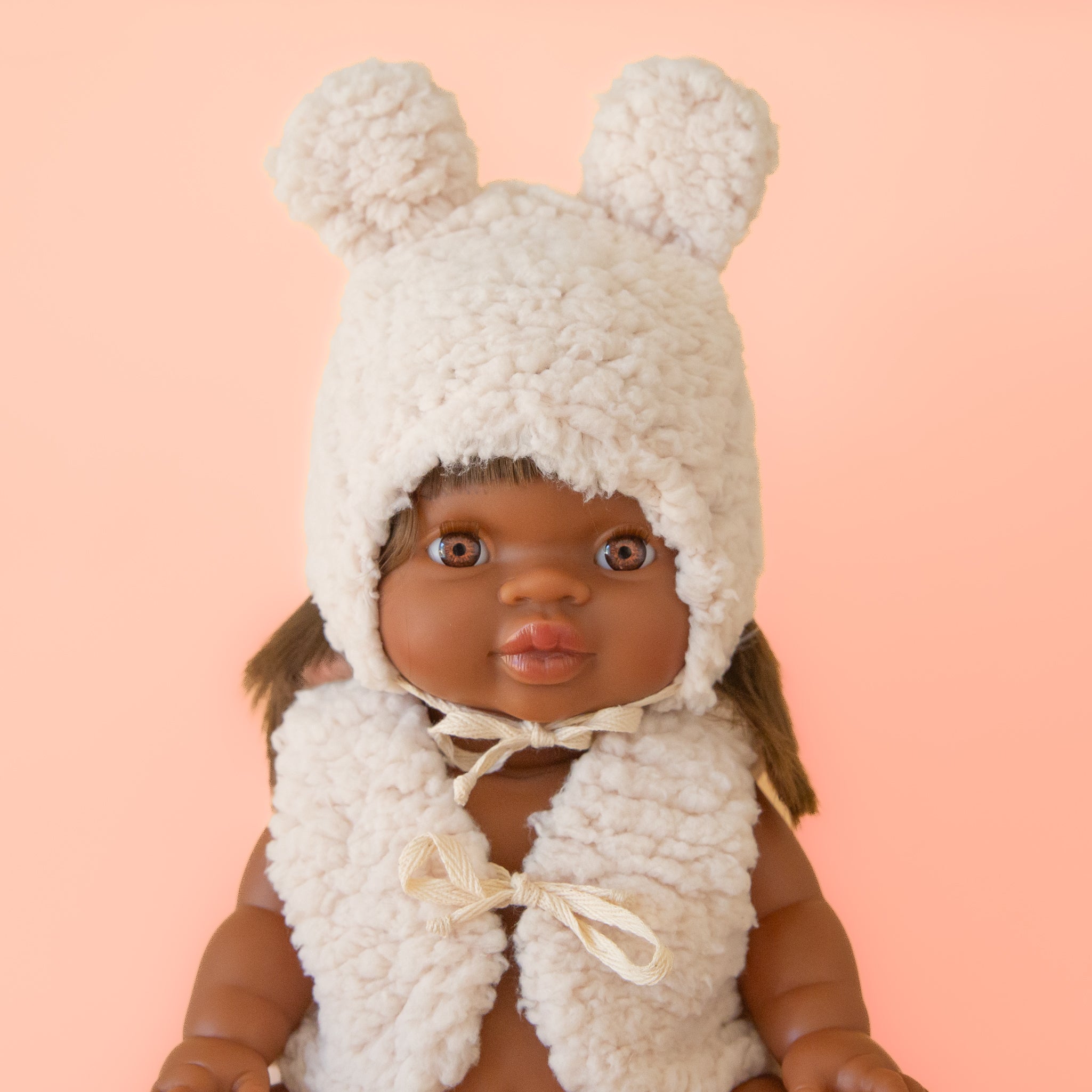 A white sherpa hat with ears on a Minikane doll. 