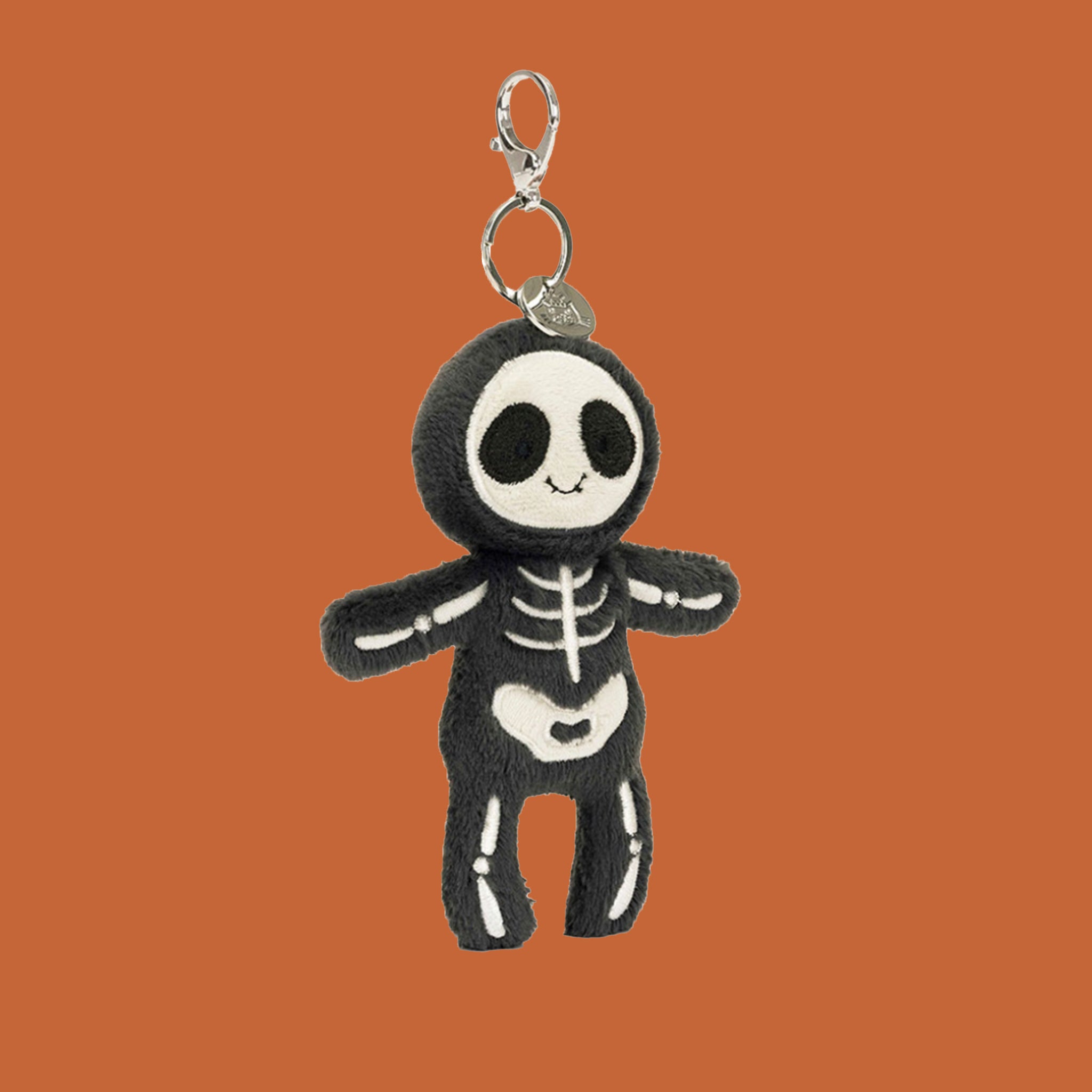 A black and white skeleton shaped stuffed toy bag charm with silver hanging loop. 