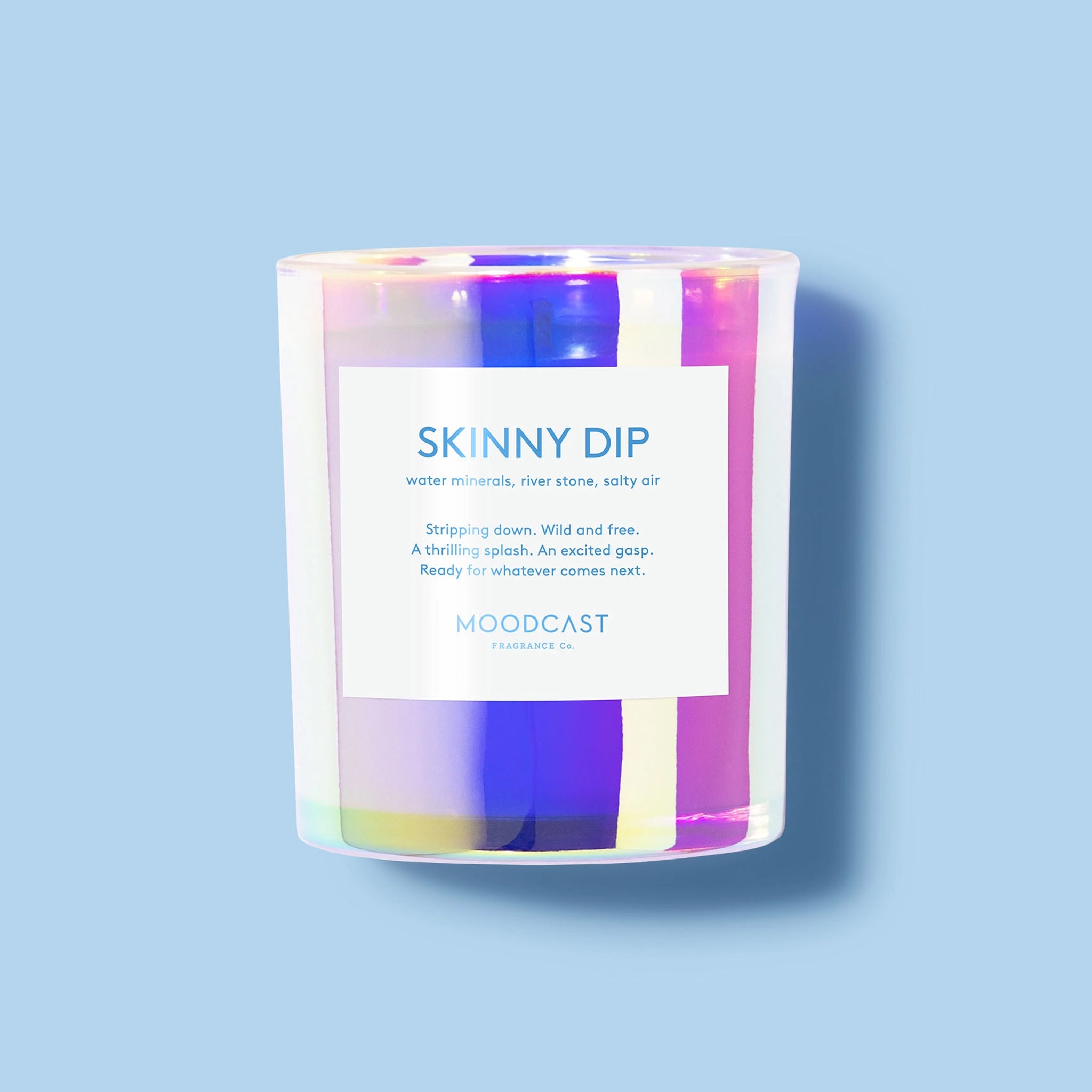 An iridescent glass candle with a white label that reads "Skinny Dip". 