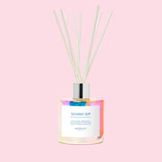 A multi colored glass diffuser with wood reeds and text on the label that reads, "Skinny Dip". 