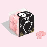 An acrylic cube with a skeleton design and filled with pink gummy skull shaped candies. 