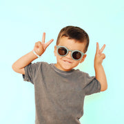 On a blue background is a model wearing a pair of light green round sunglasses. 