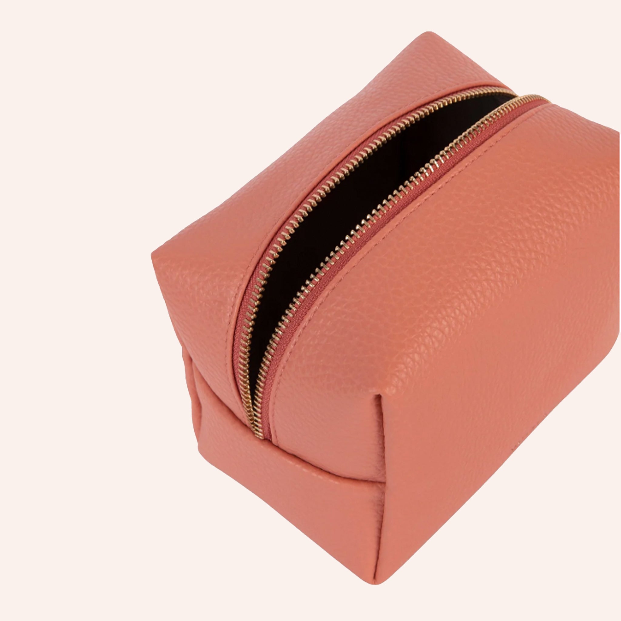 A coral vegan leather toiletry case with a handle on one side and a zipper closure across the top.