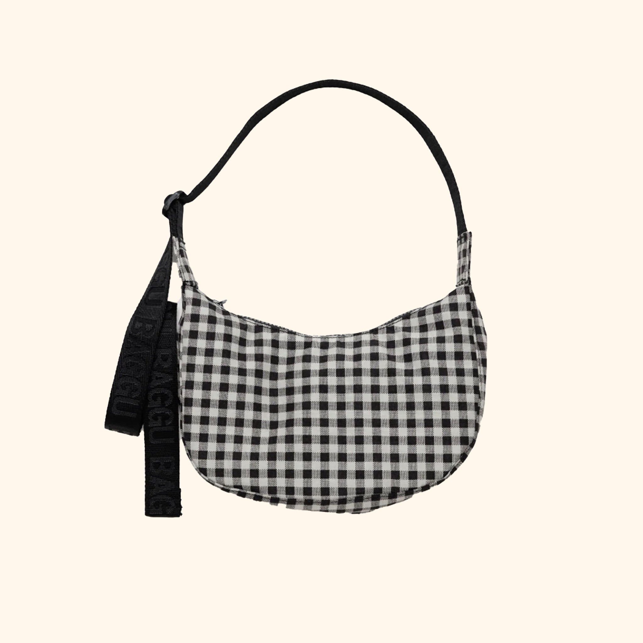 A small crescent shaped nylon back with a black and white gingham print and an adjustable strap. 