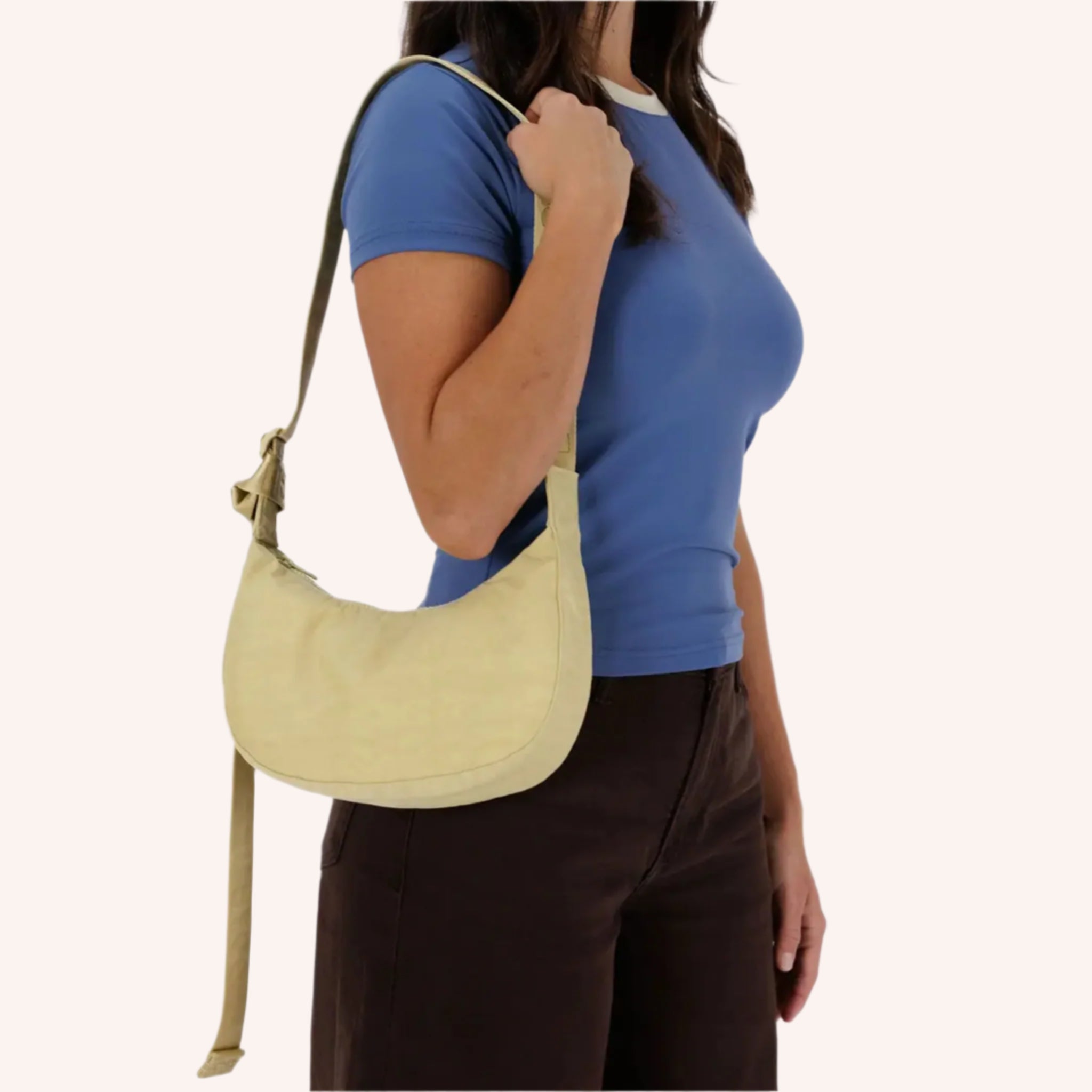 A light yellow crescent shaped nylon handbag with an adjustable strap.