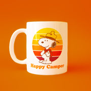 A white mug with a yellow orange and red graphic of Snoopy as a Beagle Scout and text underneath that reads, 'Happy Camper'