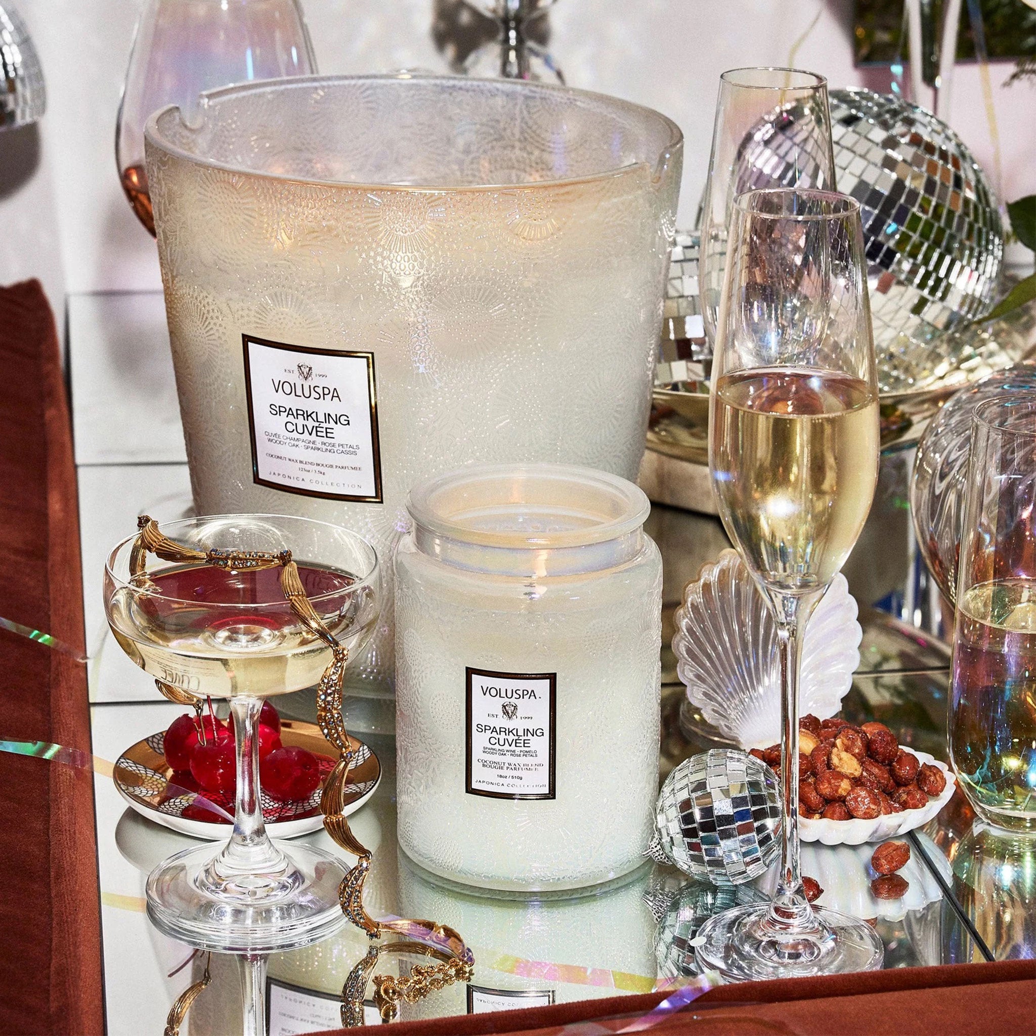 A white glass decorative candle jar with the classic Voluspa logo in the center that says the scent of the candle which in this case is &quot;Sparkling Cuvee&quot;.