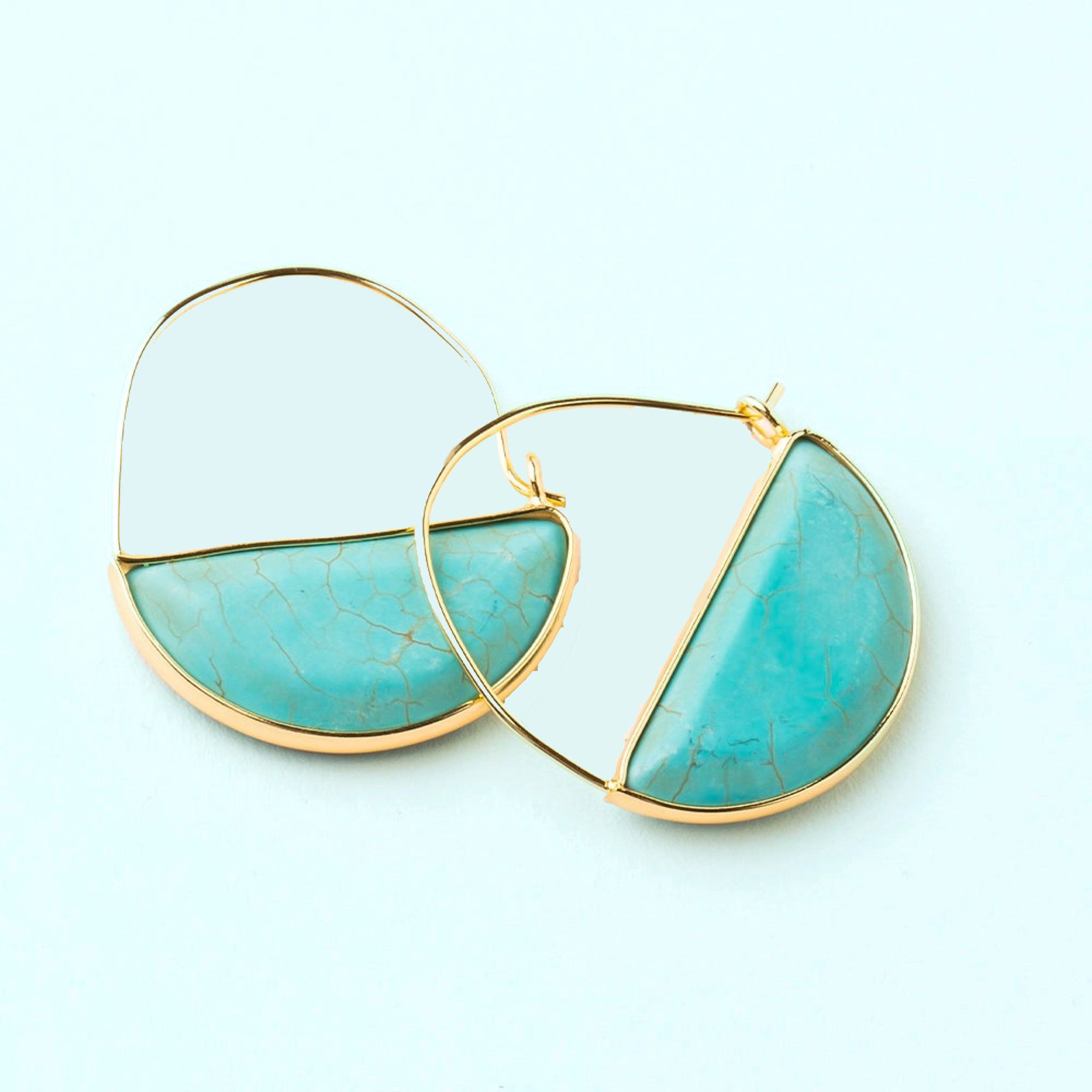 In front of a cream background is a pair of gold earrings. The top is a thin gold hoop. The bottom is a turquoise half circle with a gold border.