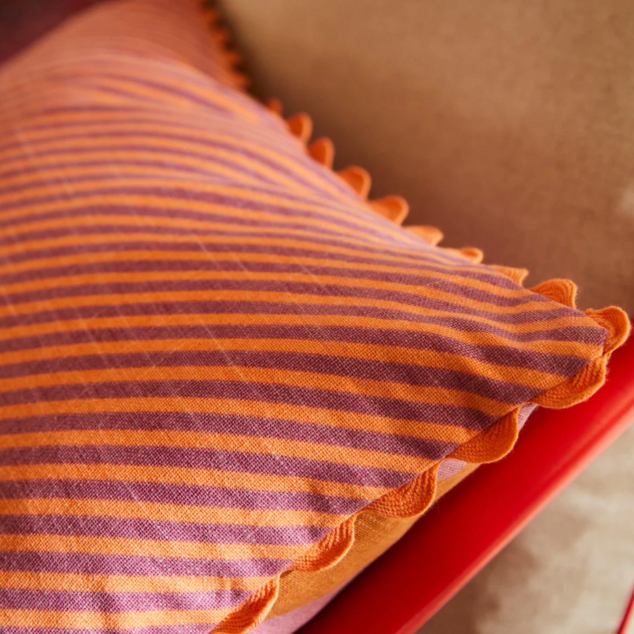 A pink and orange striped pillow with a smaller stripe on the other side and a scalloped edge. 