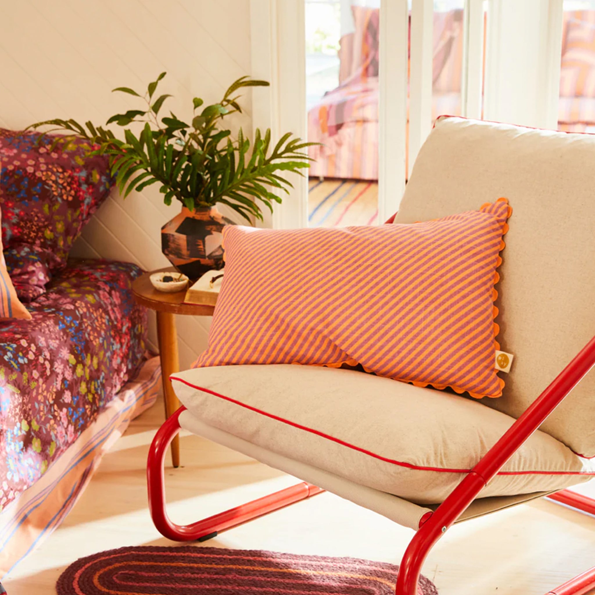 A pink and orange striped pillow with a smaller stripe on the other side and a scalloped edge. 