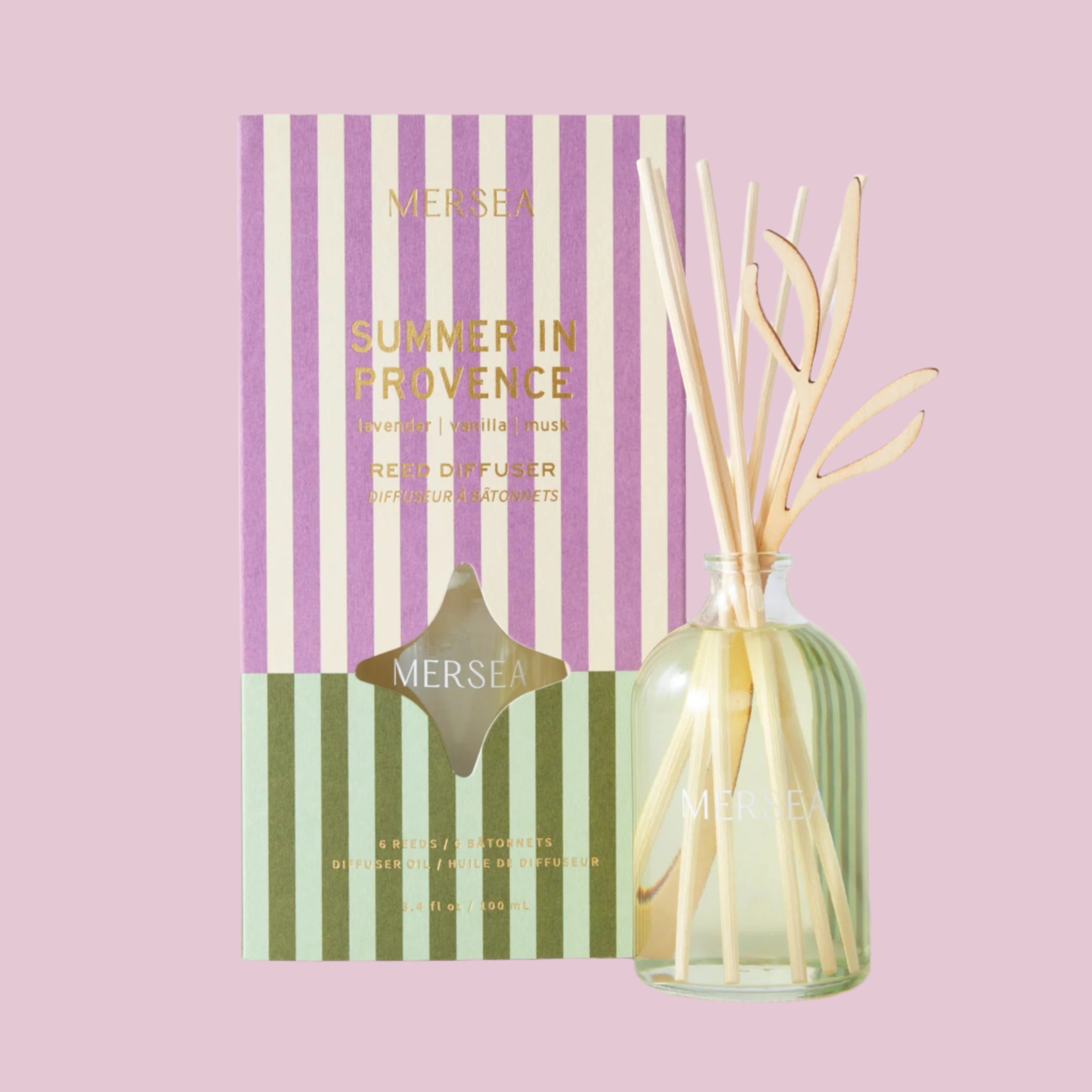 A purple and green striped box with a small glass diffuser with wooden reeds and a clear glass bottle. 