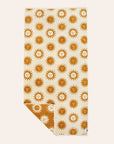 A cream and mustard yellow beach / bath towel with a sun design on the front and back, photographed here with the cream side facing up and a corner of the towel flipped over to show the opposite yellow side. 