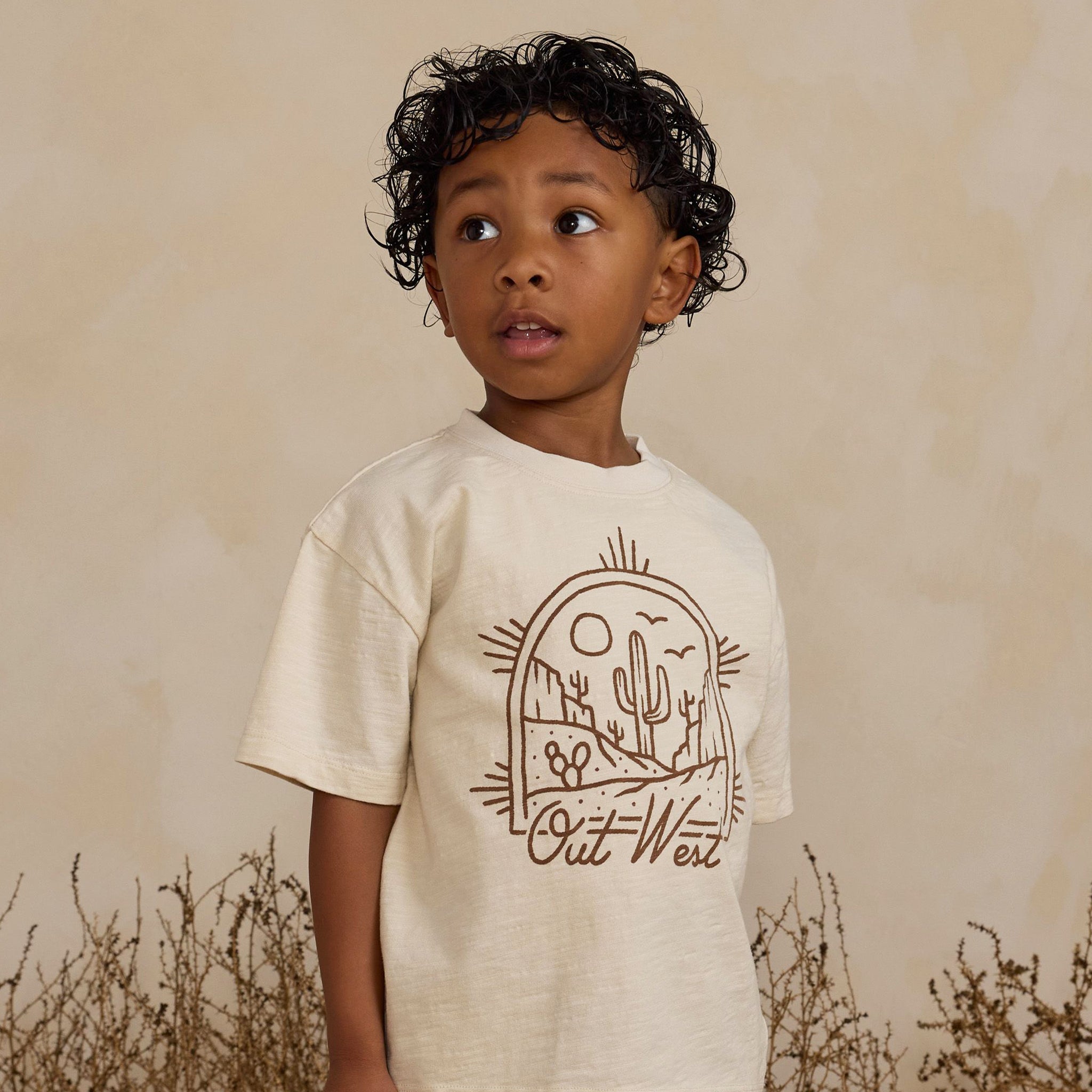 An ivory t-shirt for children with a brown western graphic on the front that reads, "Out West".