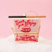 A glass ornament made to look like a pink Chinese takeout box with a pair of chopsticks across the top