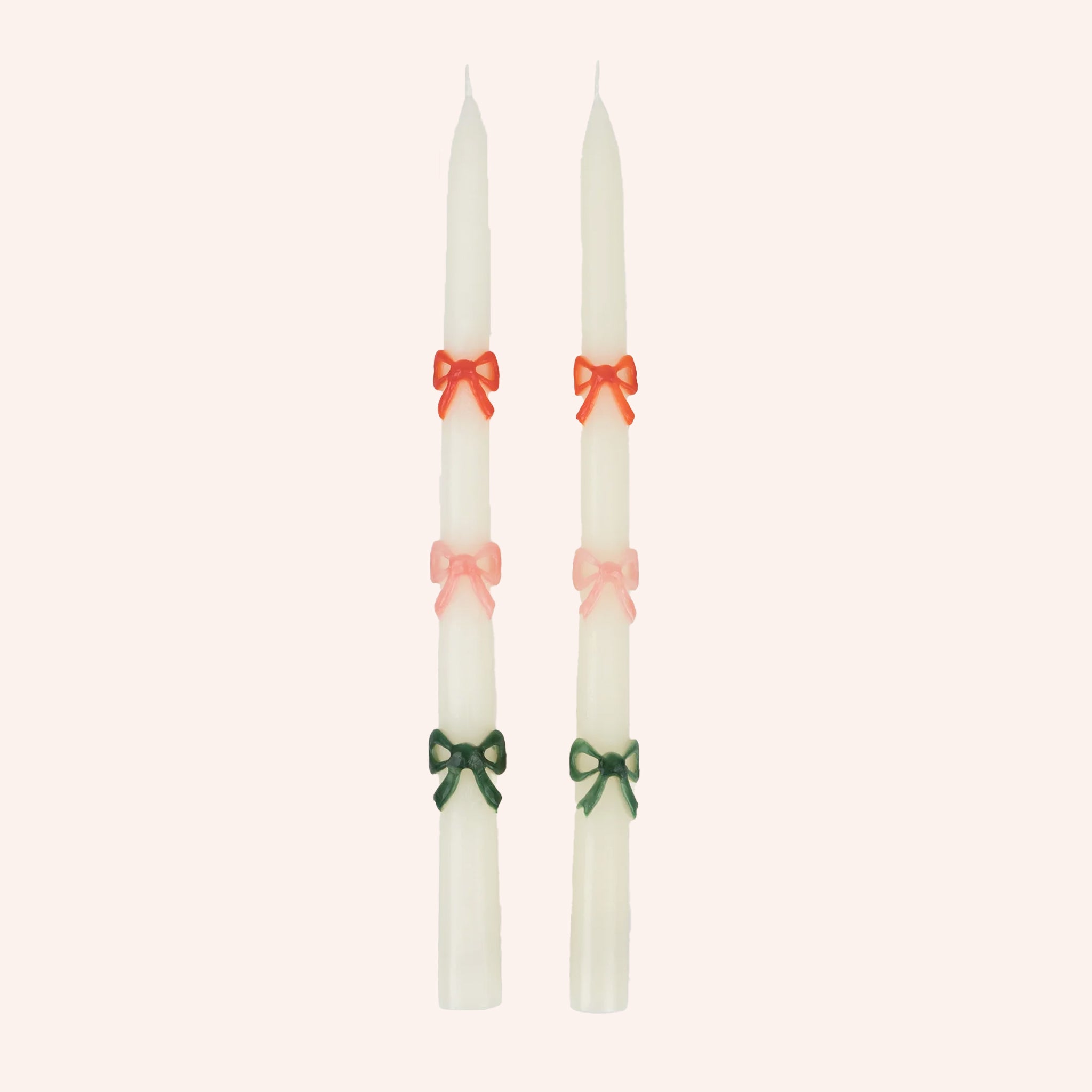 A set of two white taper candles with red, pink and green bow designs. 