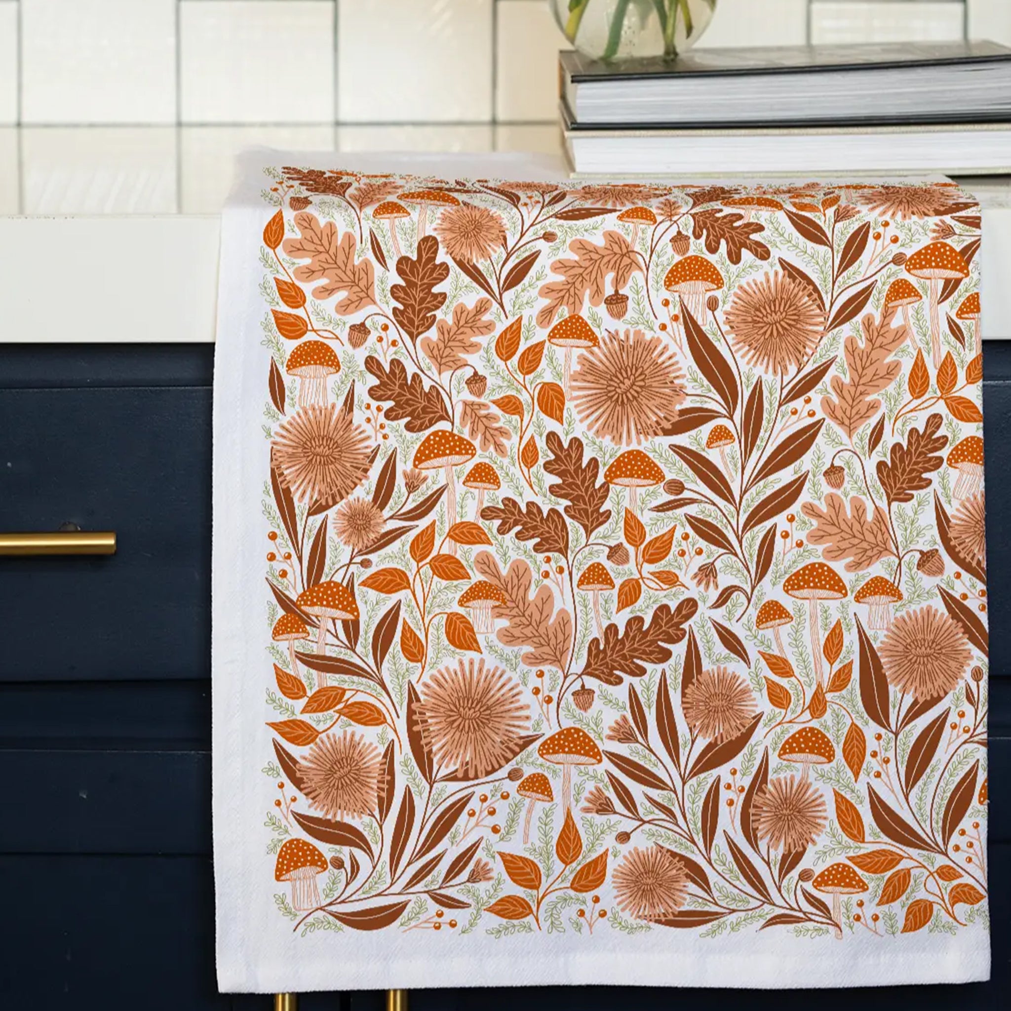 A white cotton kitchen towel with an orange woodland and floral design.