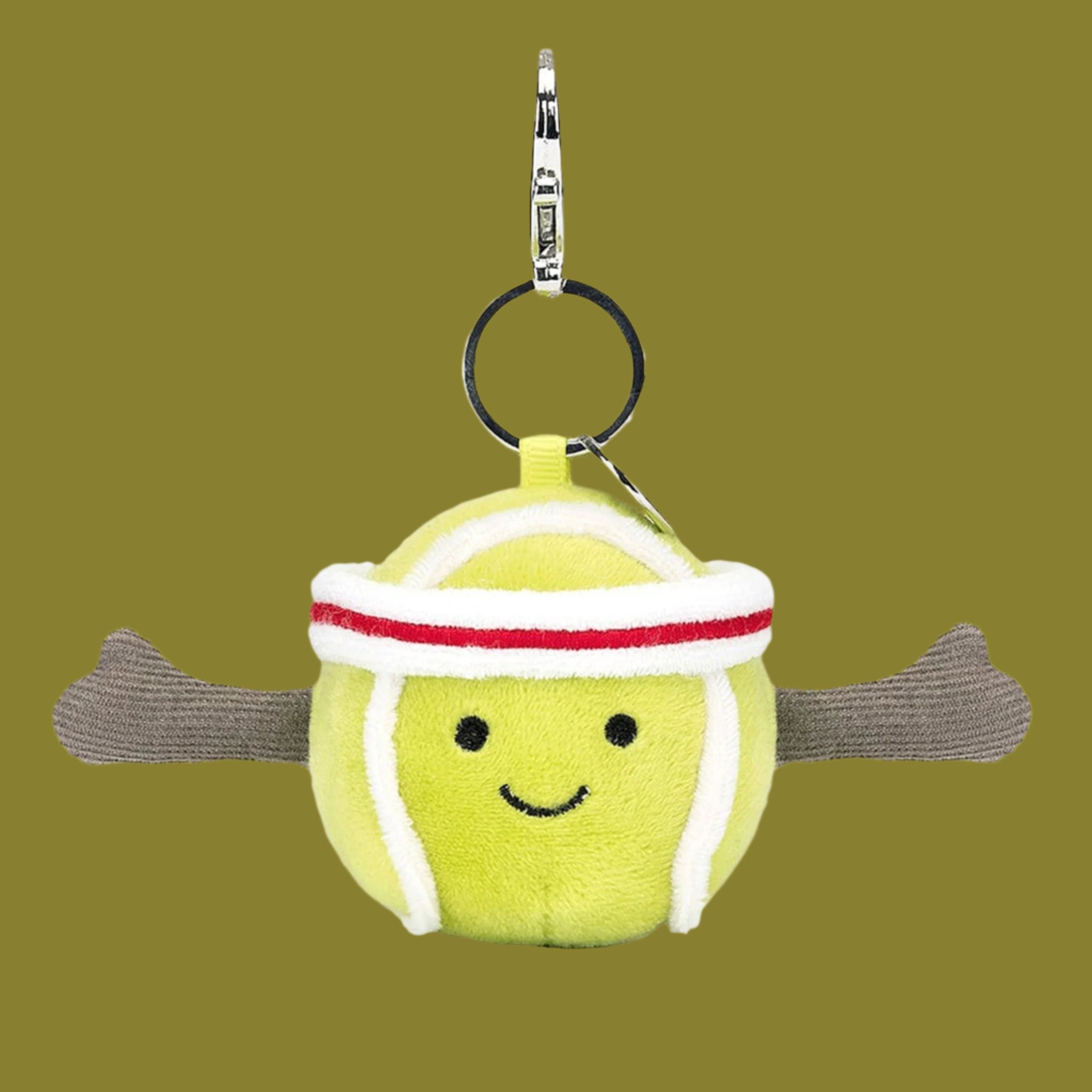 On a green background is a green tennis ball shaped bag charm with a smiling face and a silver loop for attaching.