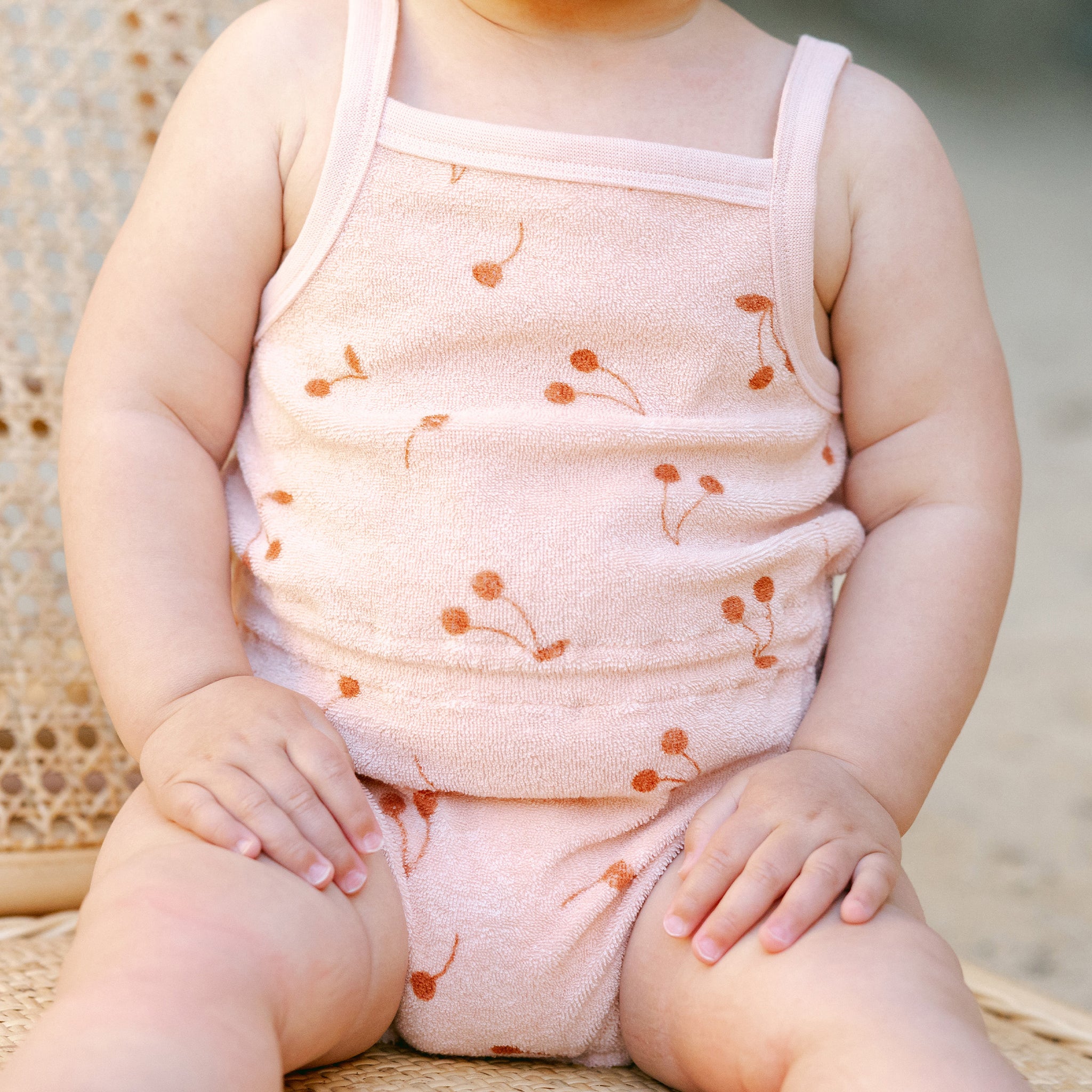 A spaghetti strap light pink terry cloth jumpsuit with a cherry print. 