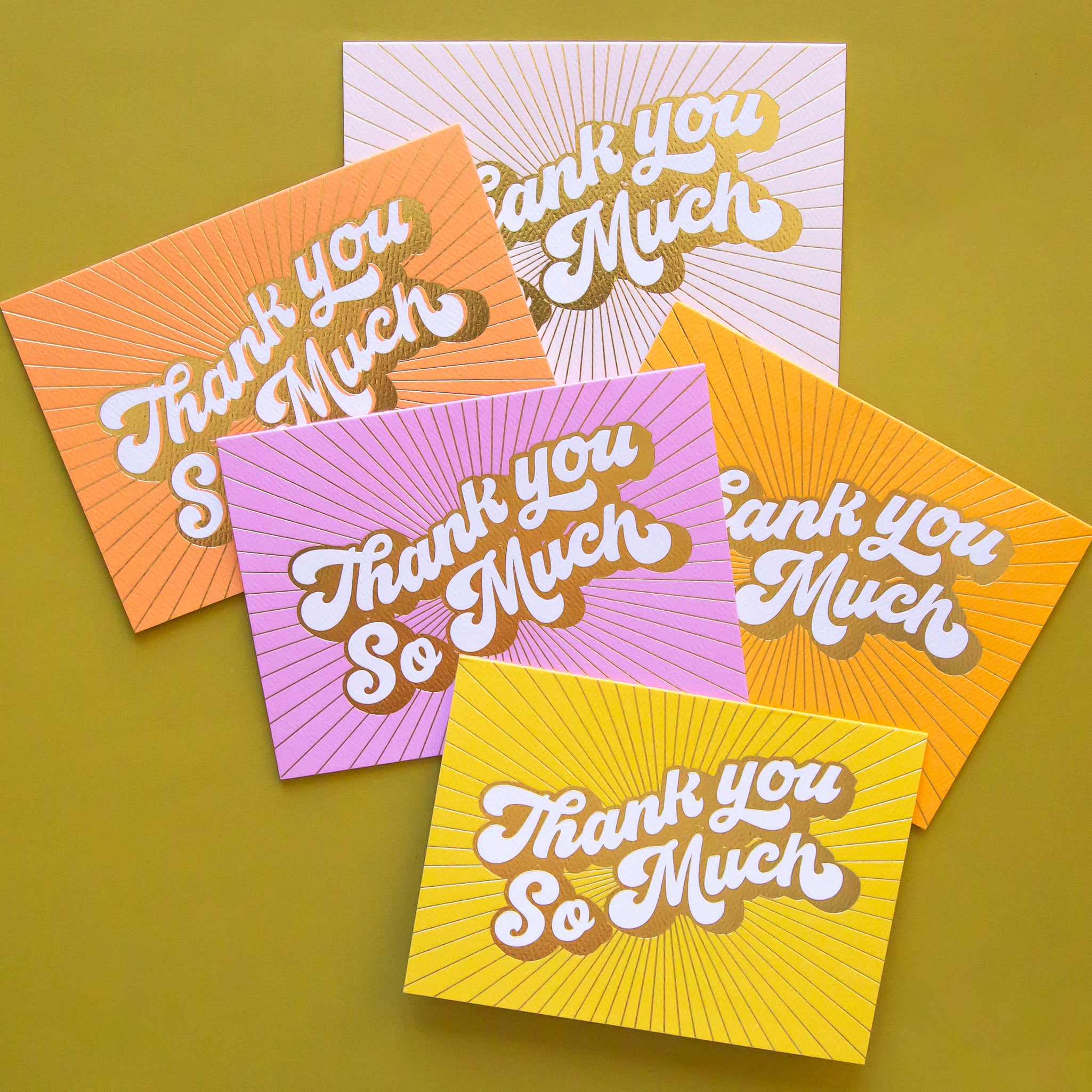 On a green background is a pack of 5 thank you cards in a variety of colors that all read, &quot;Thank You So Much&quot; in white letters and gold foiled outlined.