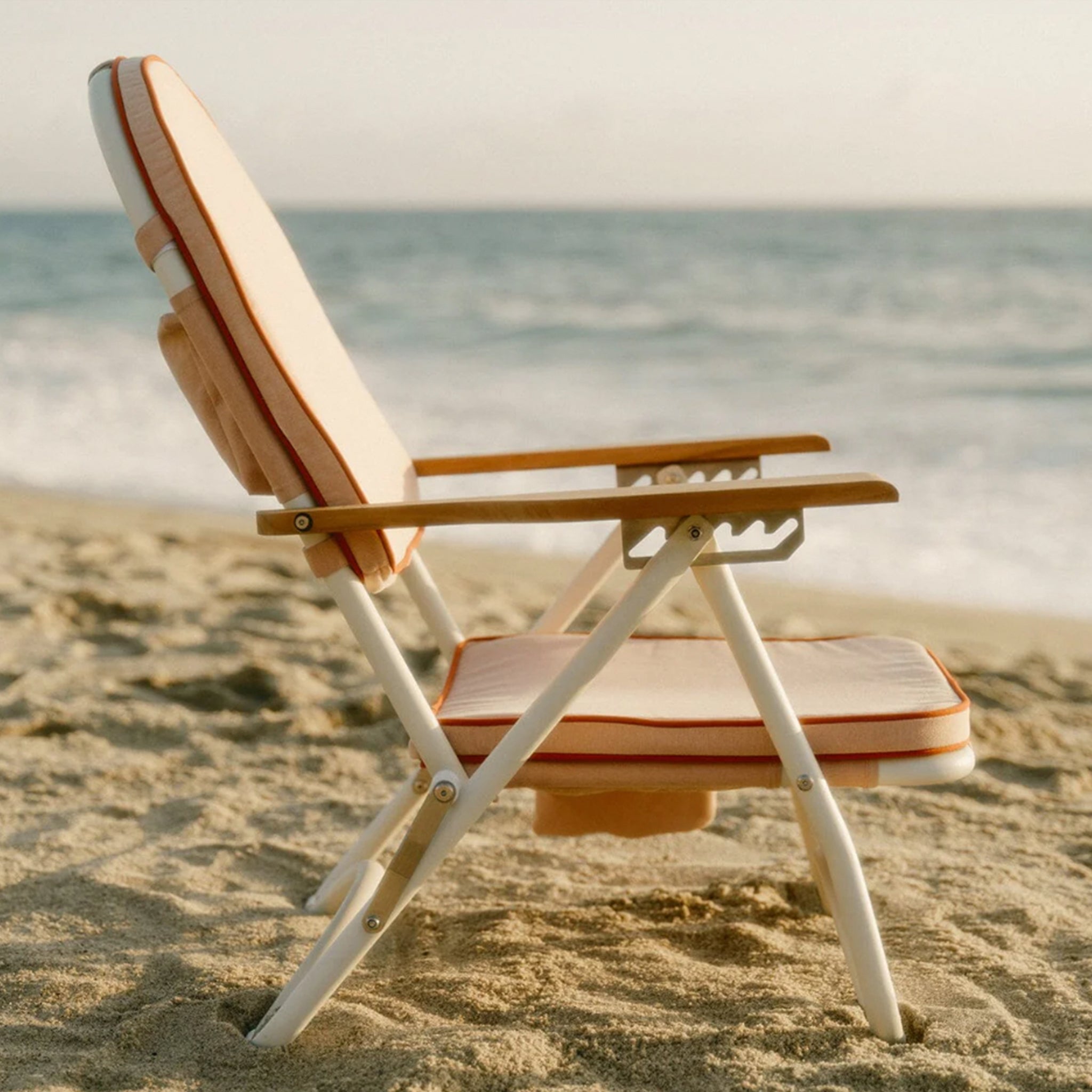 A pink arched folding beach chair with a reddish/dark pink lining around the edge and wood arm rests.