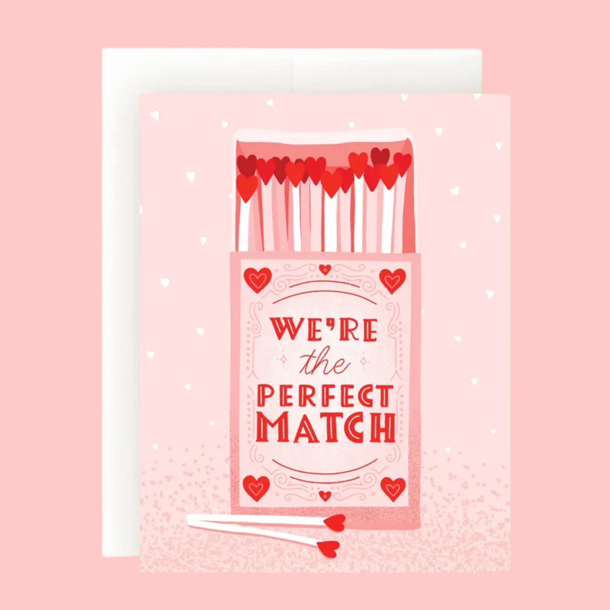 A pink card with subtle white tiny hearts and an illustration of a box of matches with wooden matches the shape of hearts and text that reads, 'We're the Perfect Match'. 